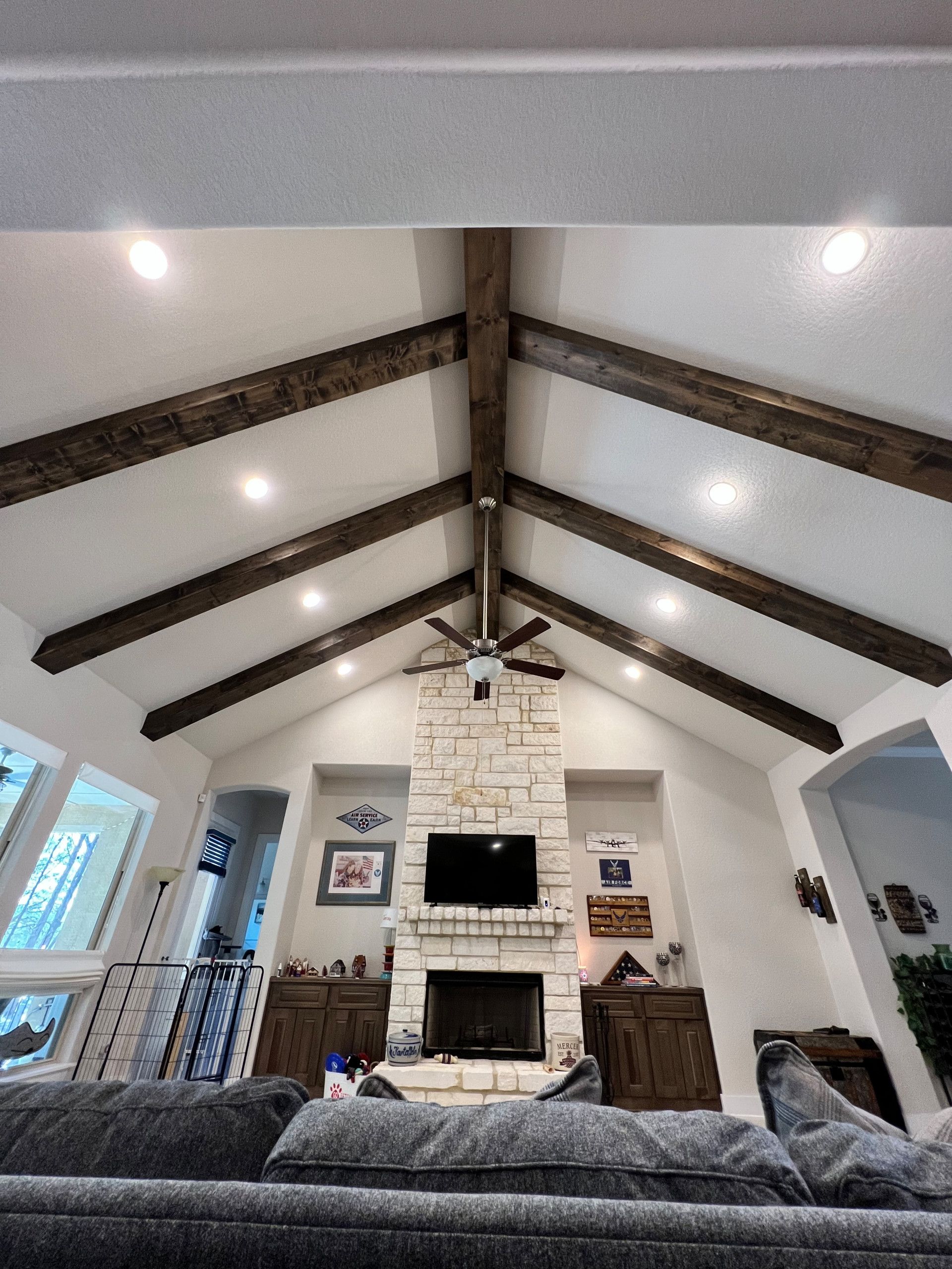 Vaulted living room ceiling with dark wood beams, recessed lighting, and a stone fireplace.