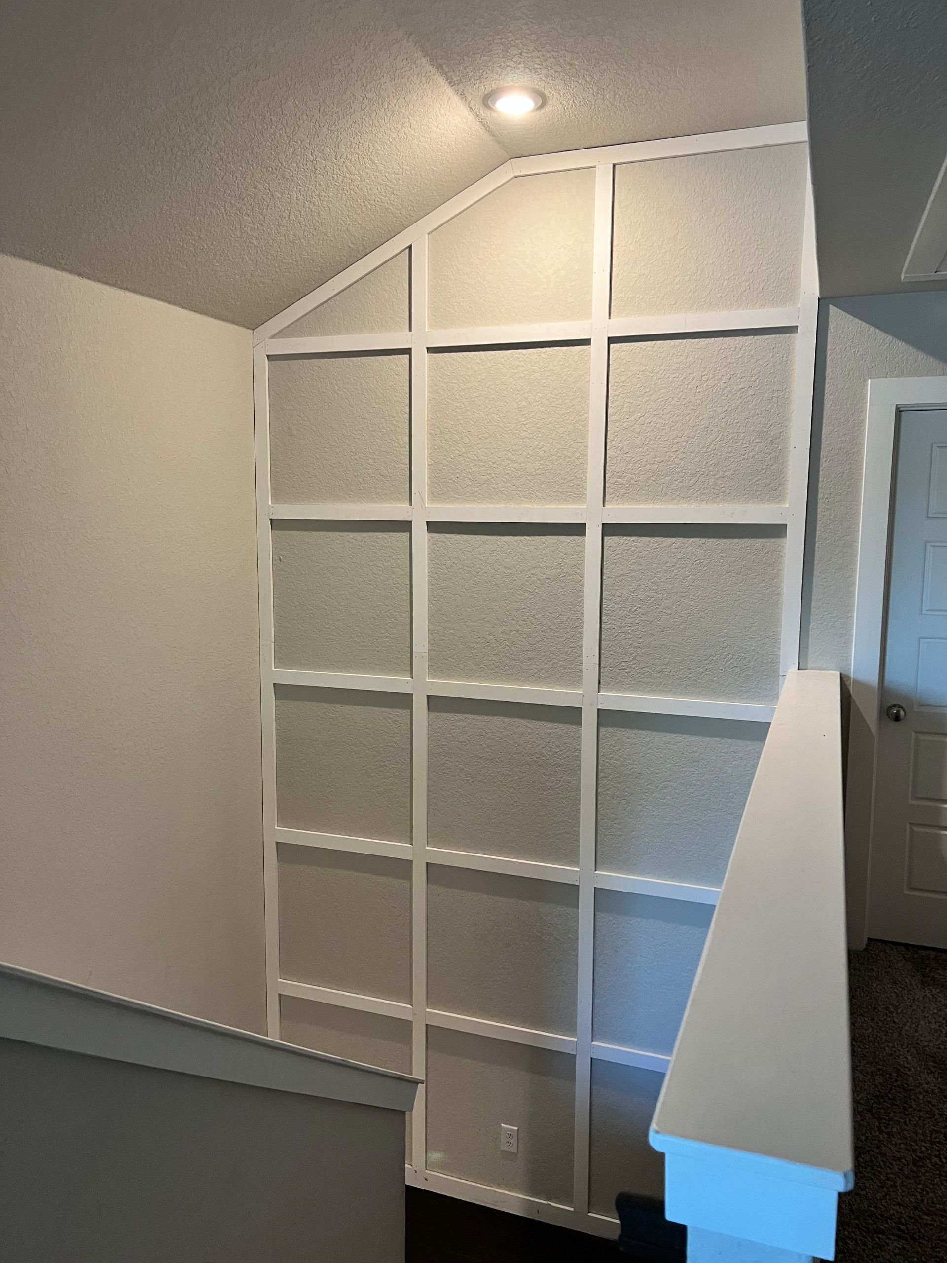 White grid-like wall decor on an angled wall between a staircase and doorway.