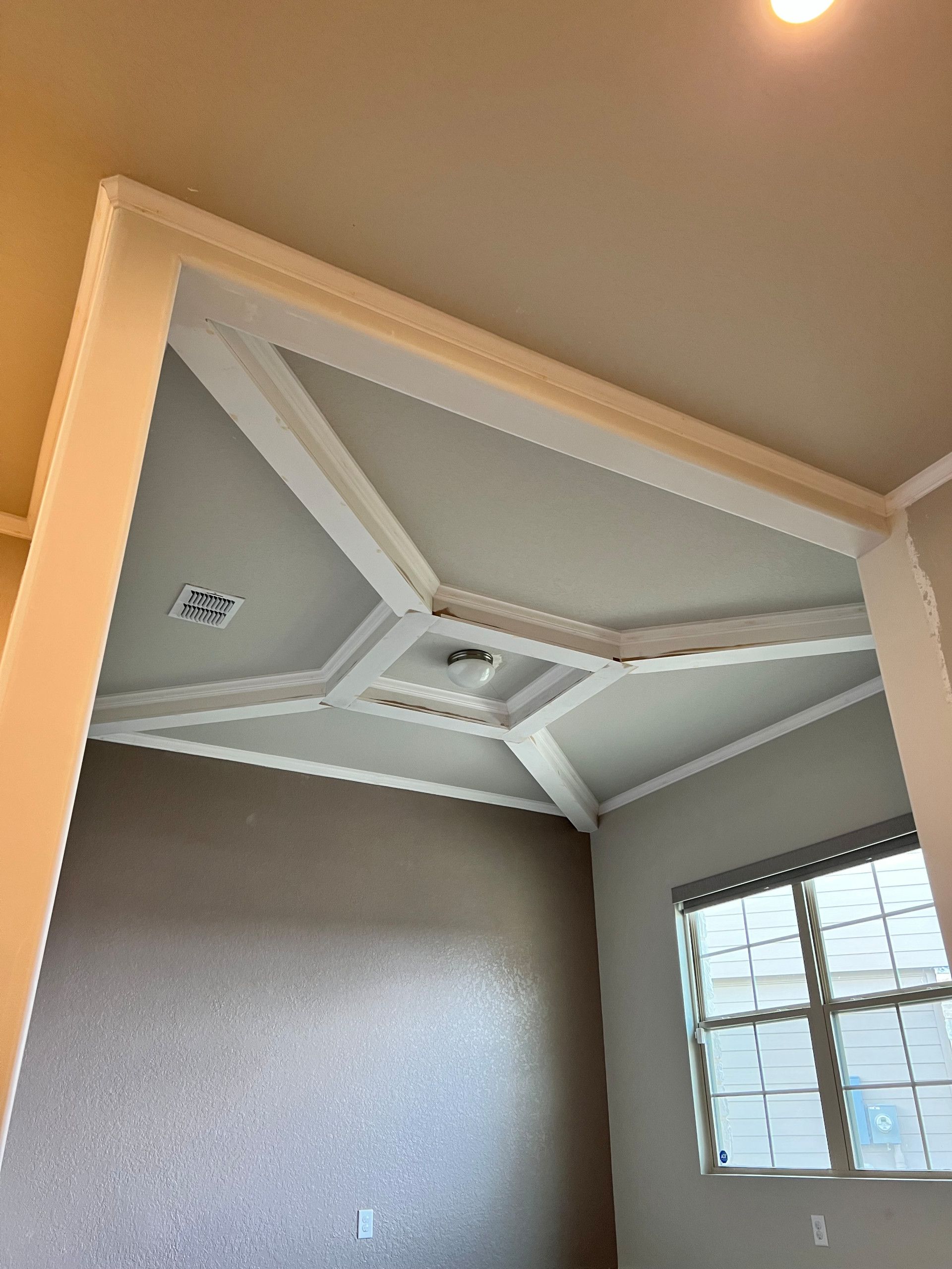 Gray room with crown molding, angled ceiling, and geometric white trim around a recessed ceiling light.