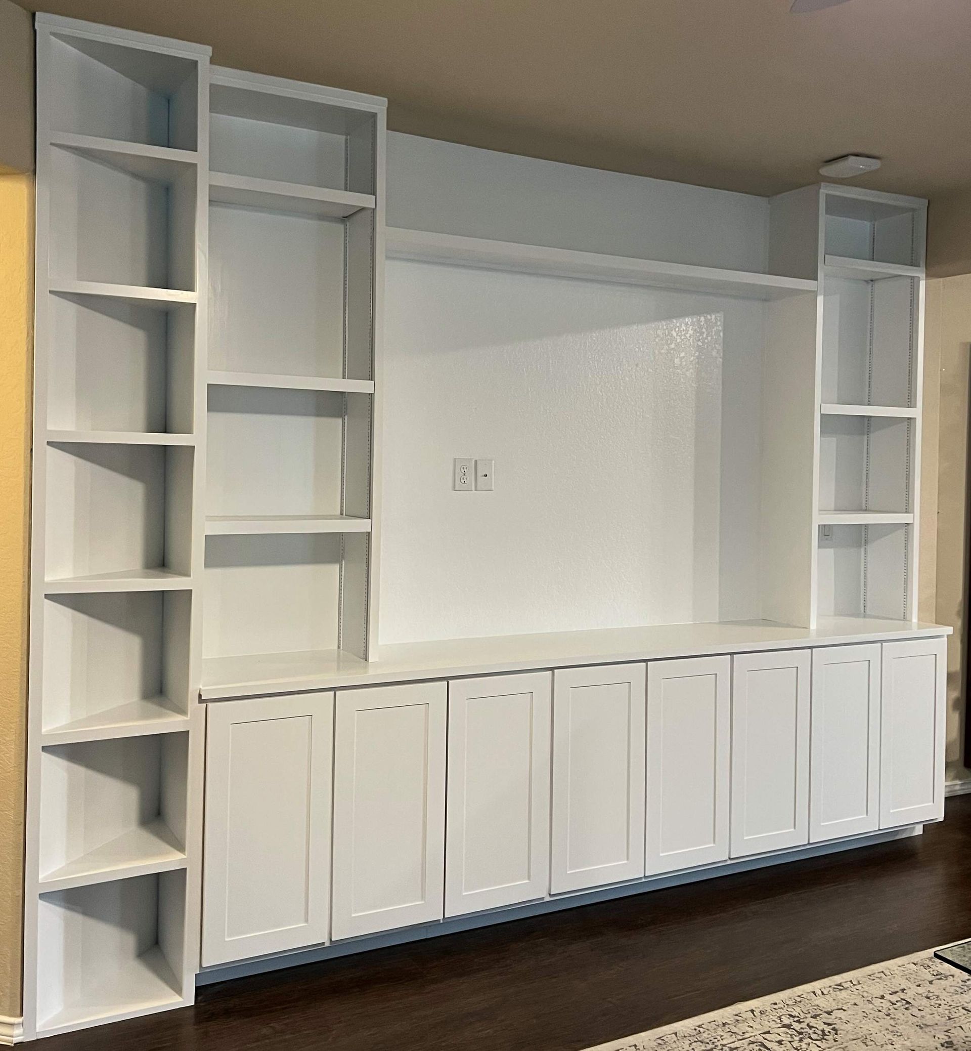 Built-in white wall unit with shelves and cabinets. It features a center space for a TV and is set against a white wall.
