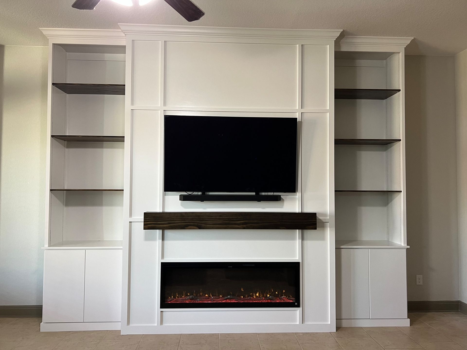 Built-in white entertainment center with a fireplace, TV, shelves, and dark wood mantel.