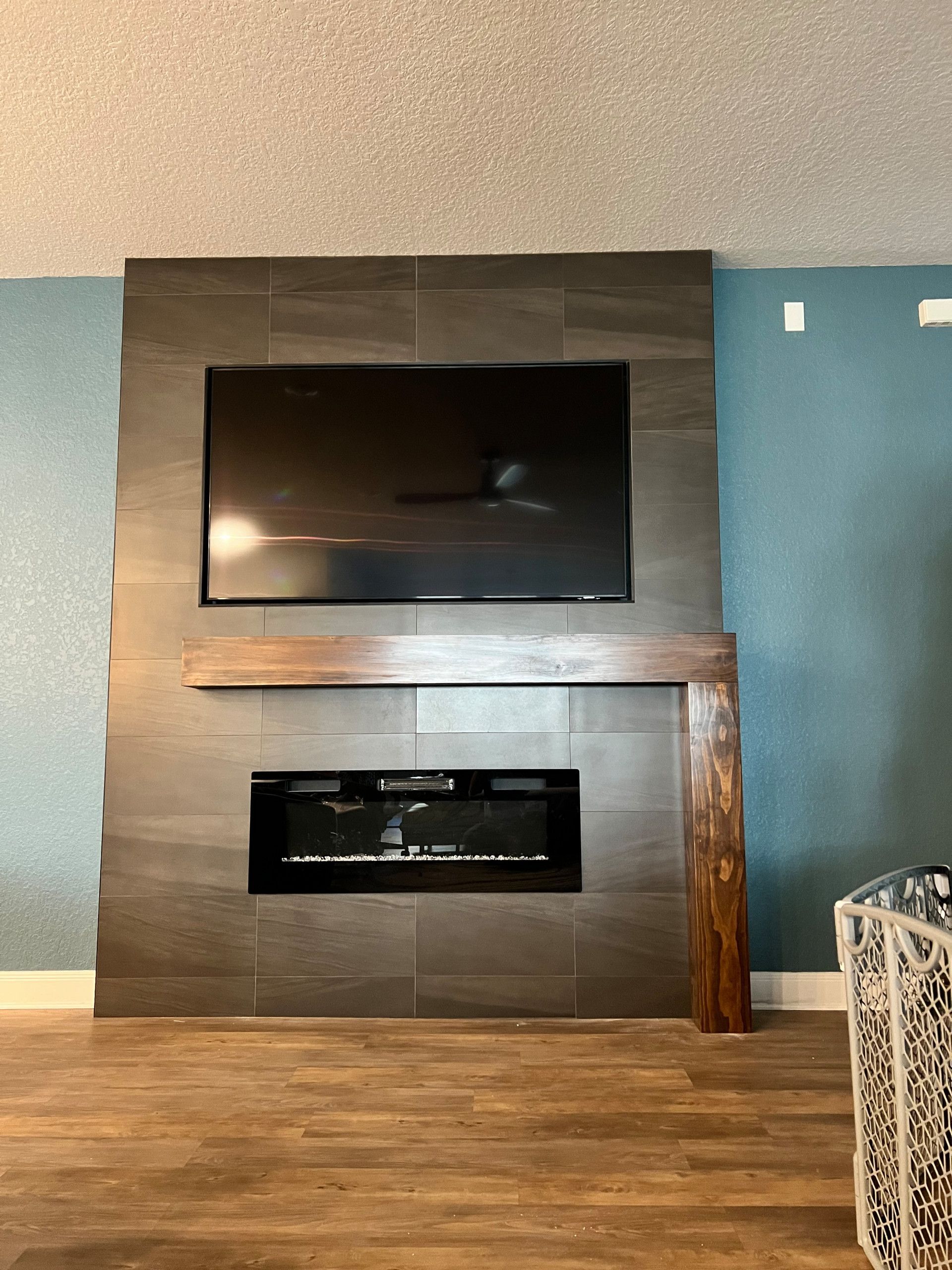 A modern fireplace with a dark tiled surround, a mounted TV, and a wood mantel on a blue wall.