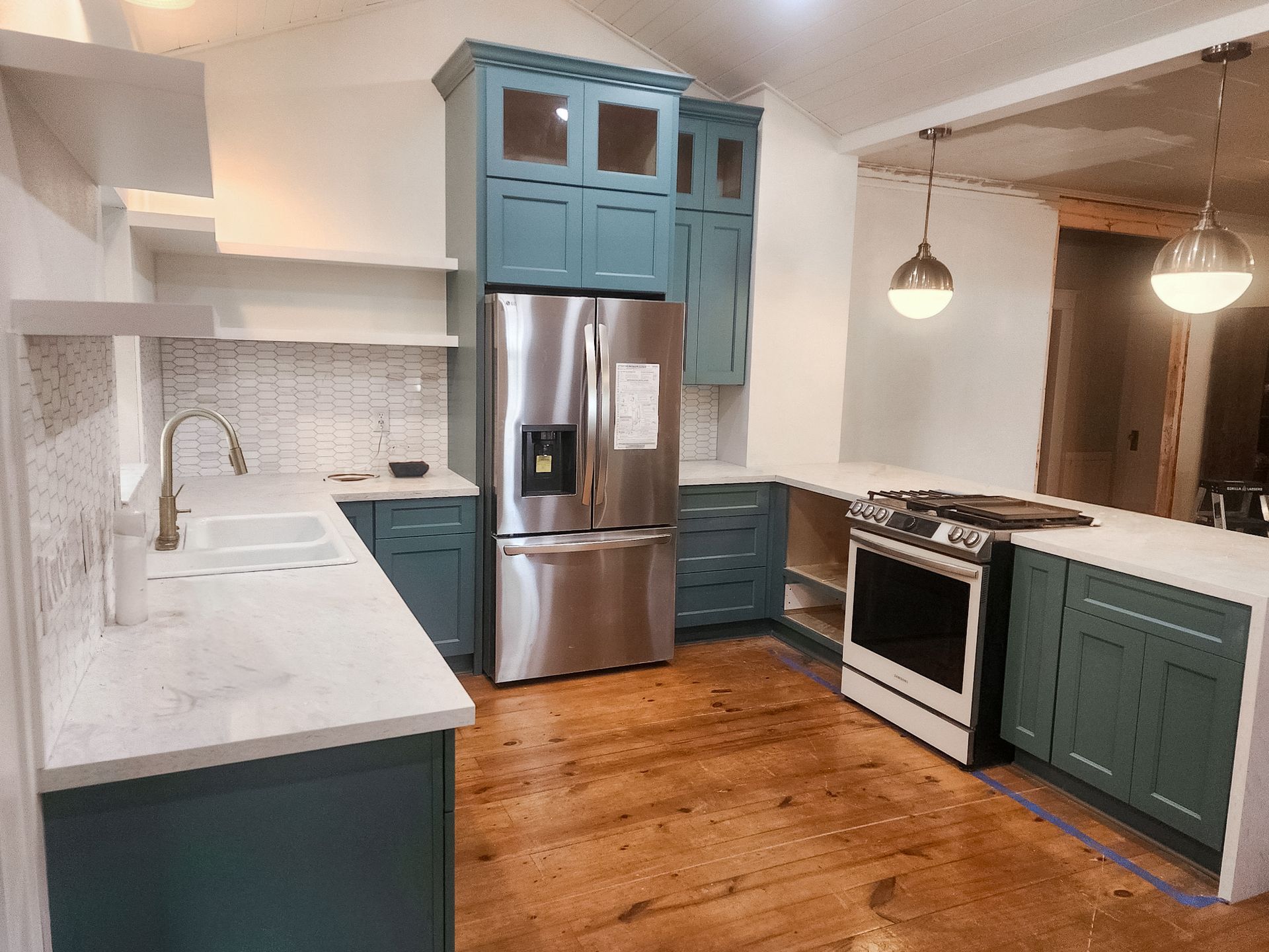 Kitchen renovation featuring teal cabinets, stainless steel refrigerator, white countertops, and wood flooring.