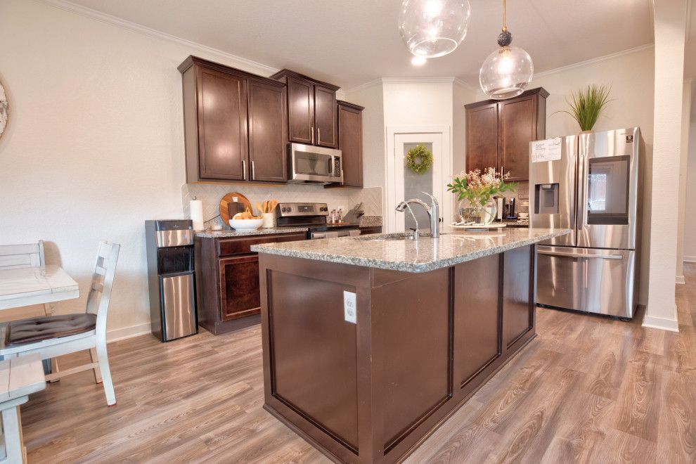 Spacious kitchen with dark cabinets, island with granite countertop, stainless steel fridge, and wooden floors.