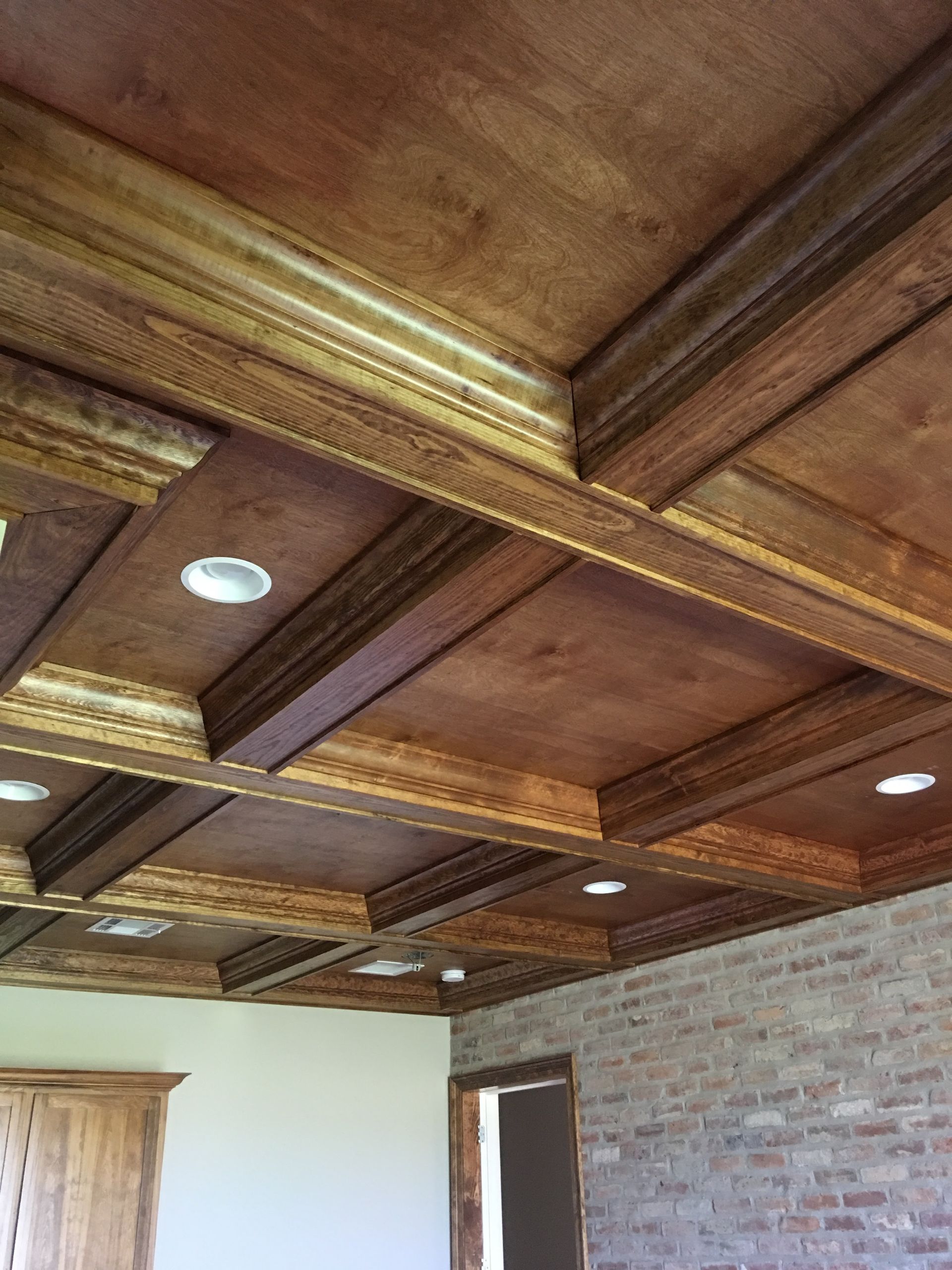 Wooden coffered ceiling with recessed lighting, over a room with brick wall.