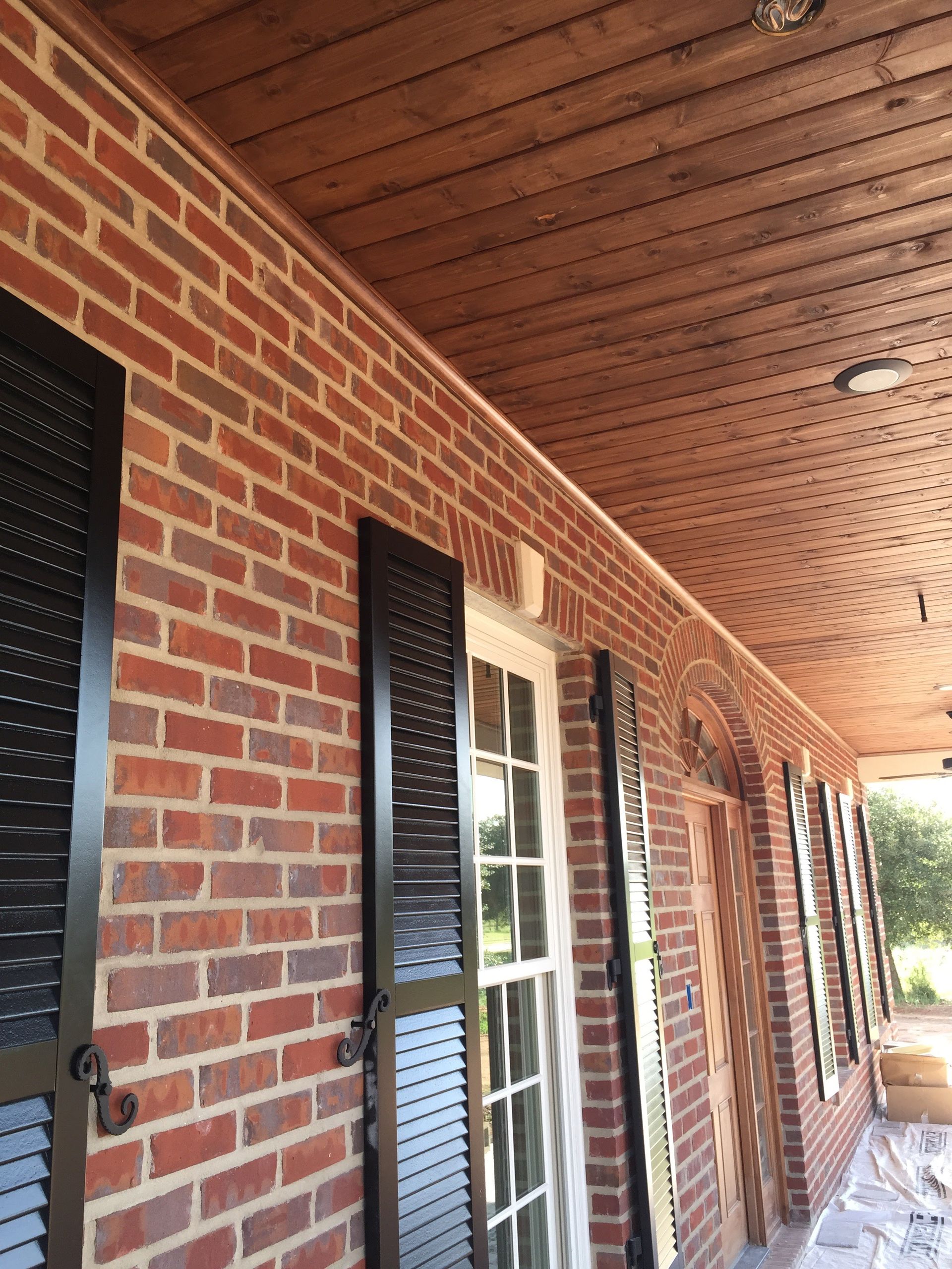 Brick building exterior with black shutters, white door, and wood ceiling.
