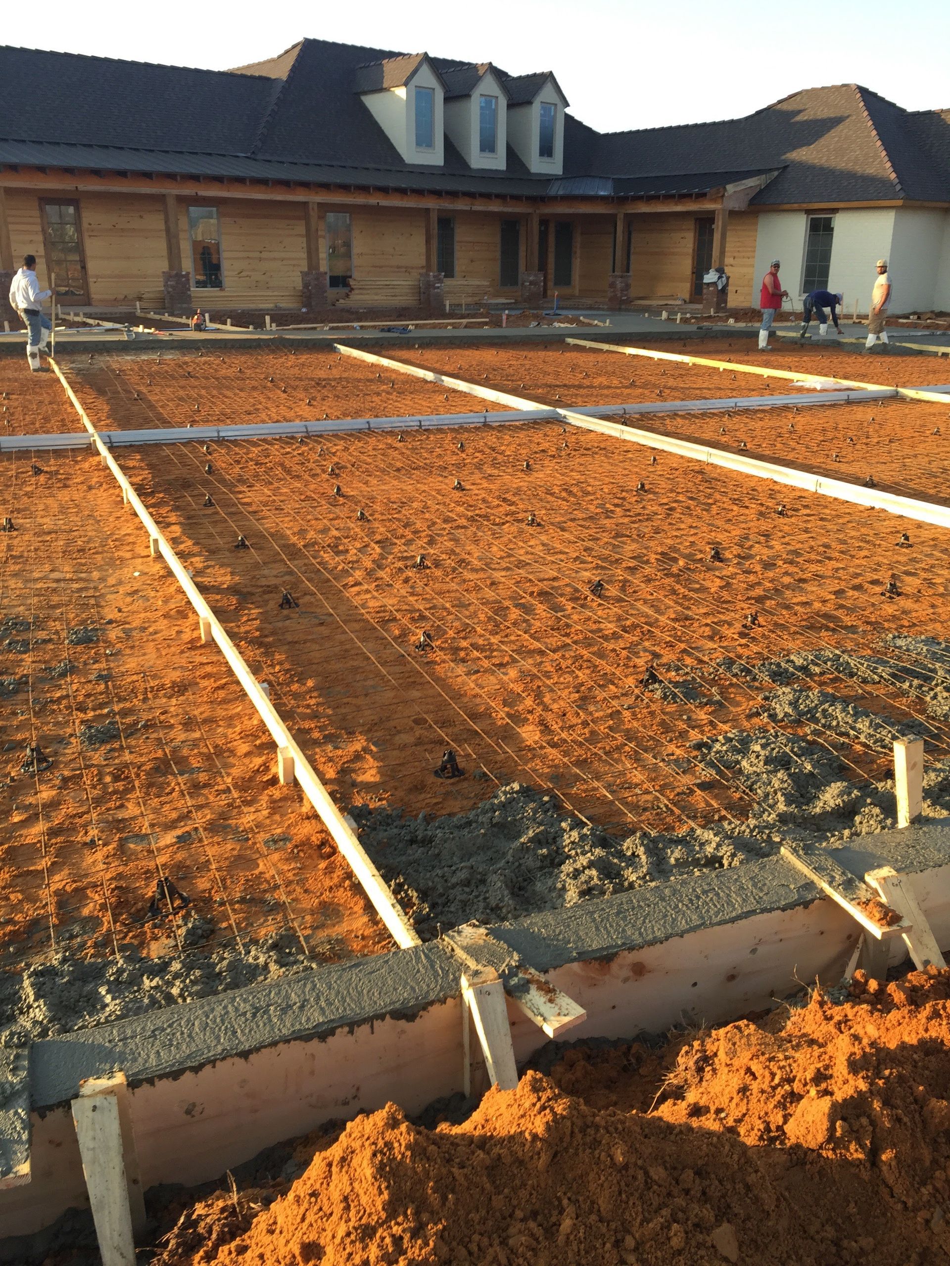 Construction site with concrete forms, rebar grid, and workers in front of a large building.