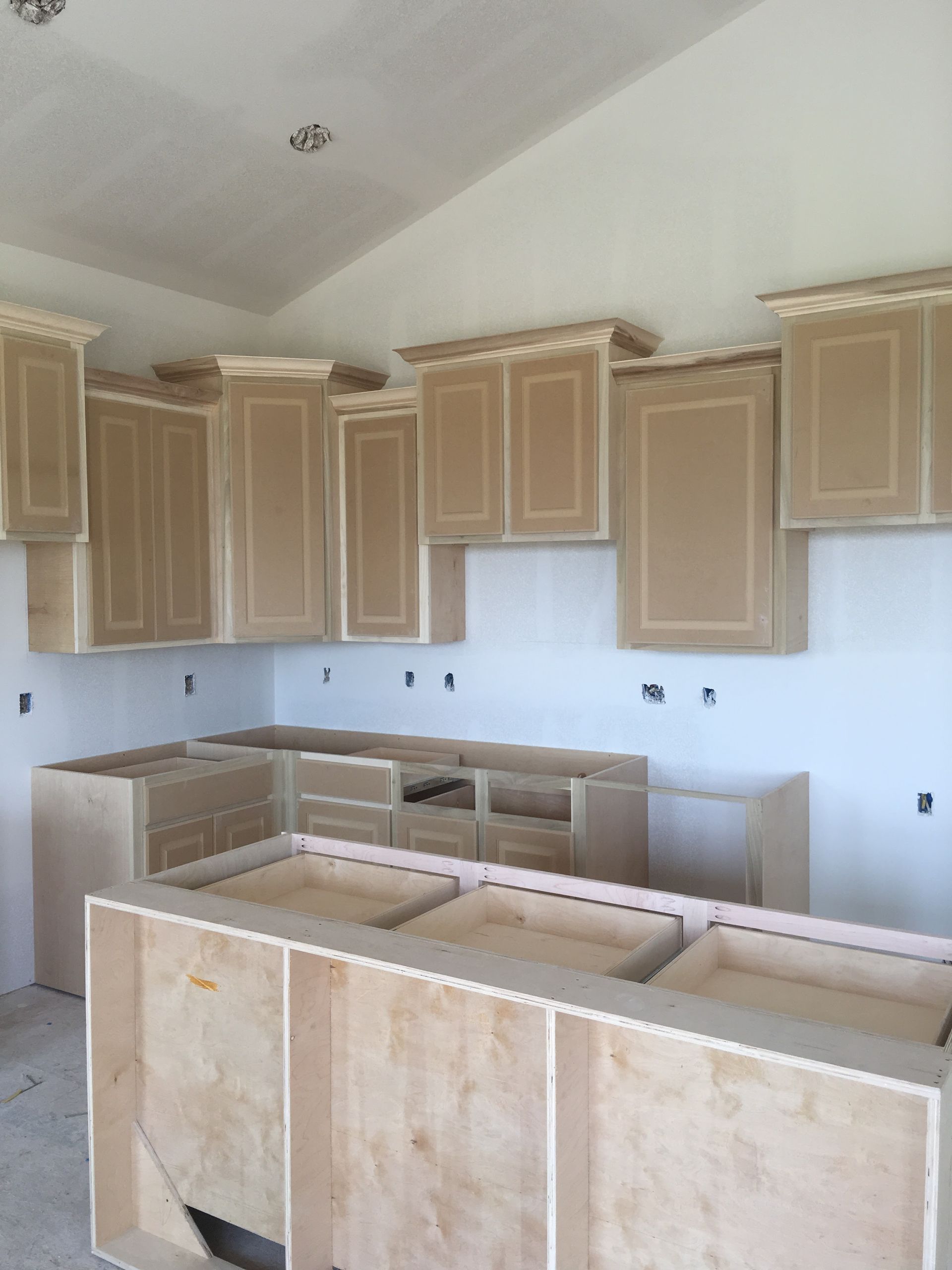 Unfinished kitchen with light wood cabinets and island under construction, set against white walls and ceiling.