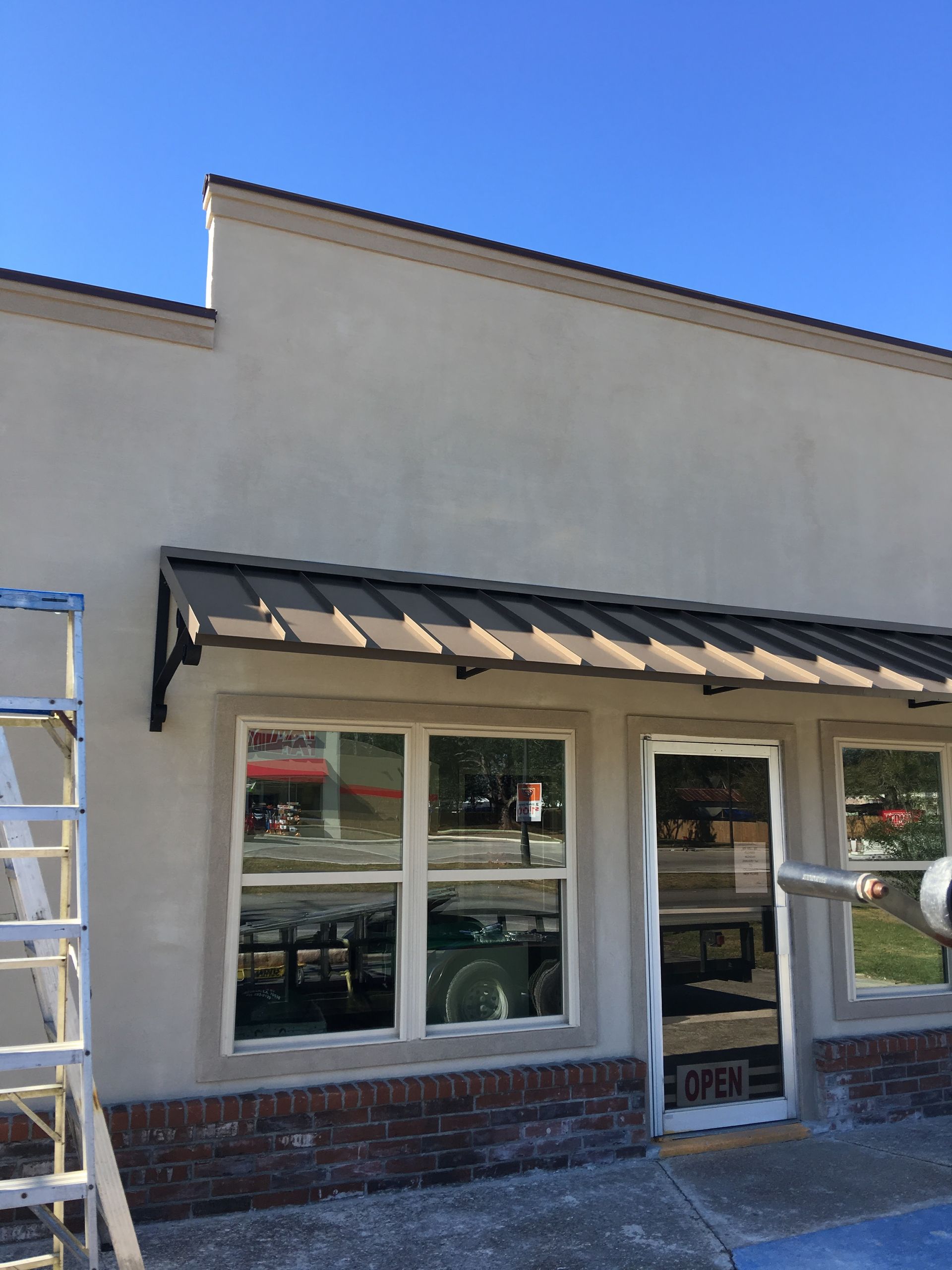 Building exterior with awning over windows and door. Beige walls, brown awning, blue sky.