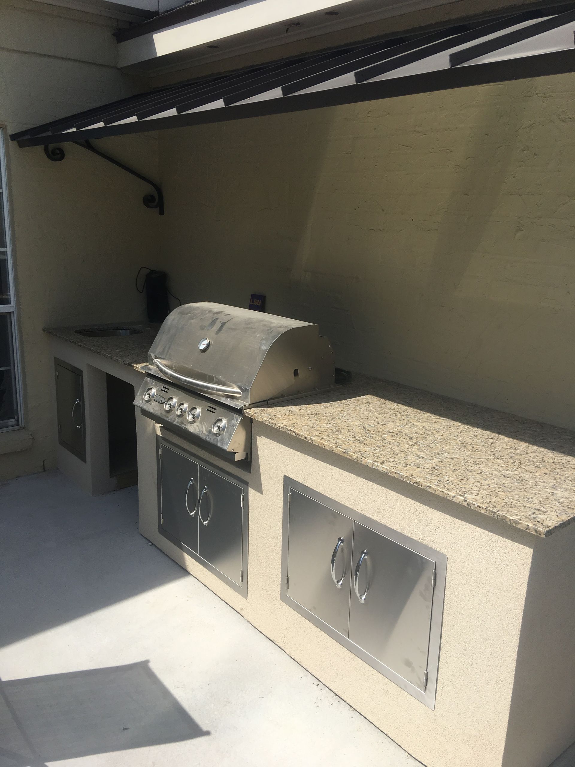 Outdoor kitchen with stainless steel grill and cabinets on a concrete countertop.