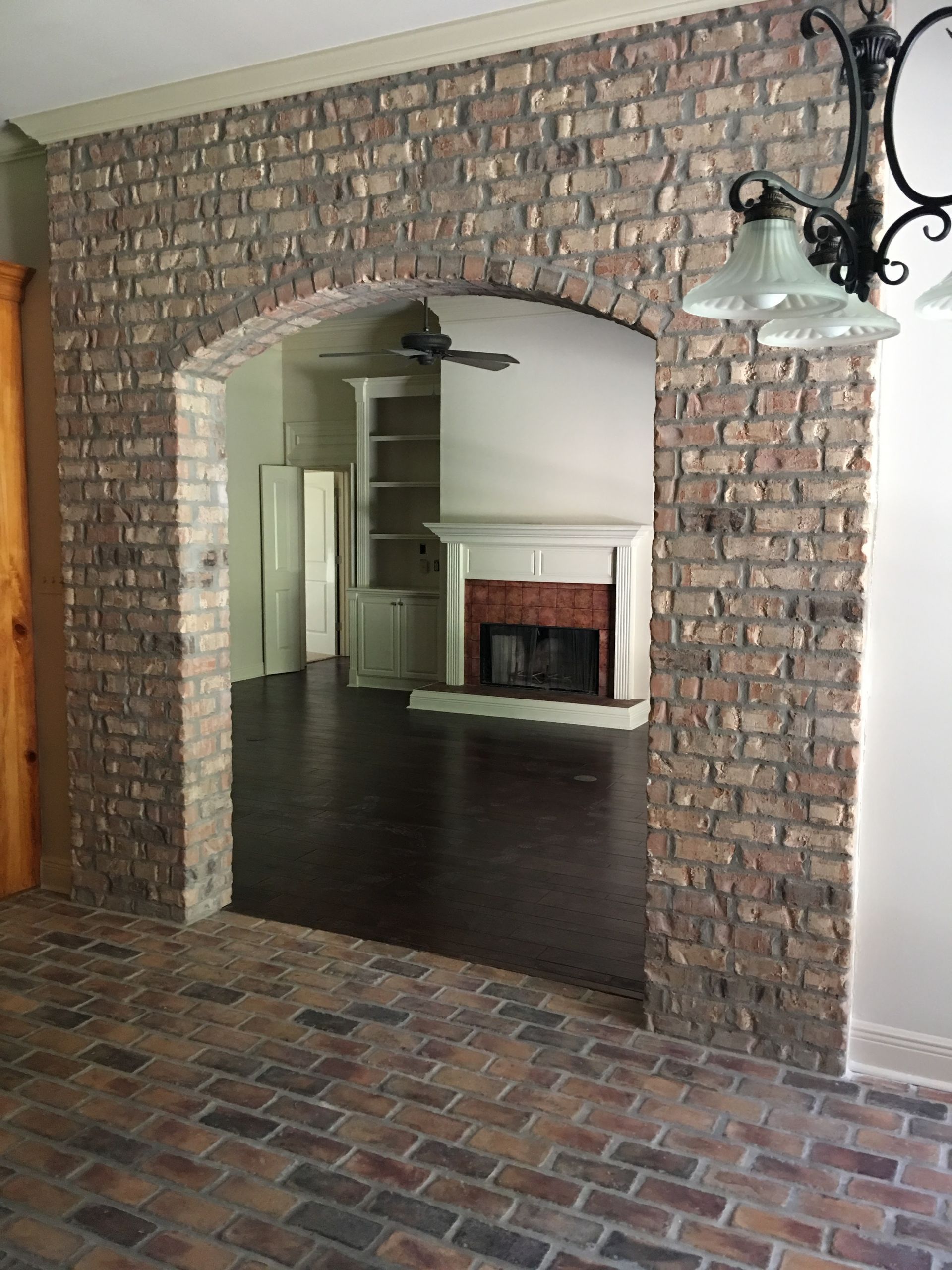 Brick archway leading to a room with a fireplace. Brick flooring and a chandelier are also visible.