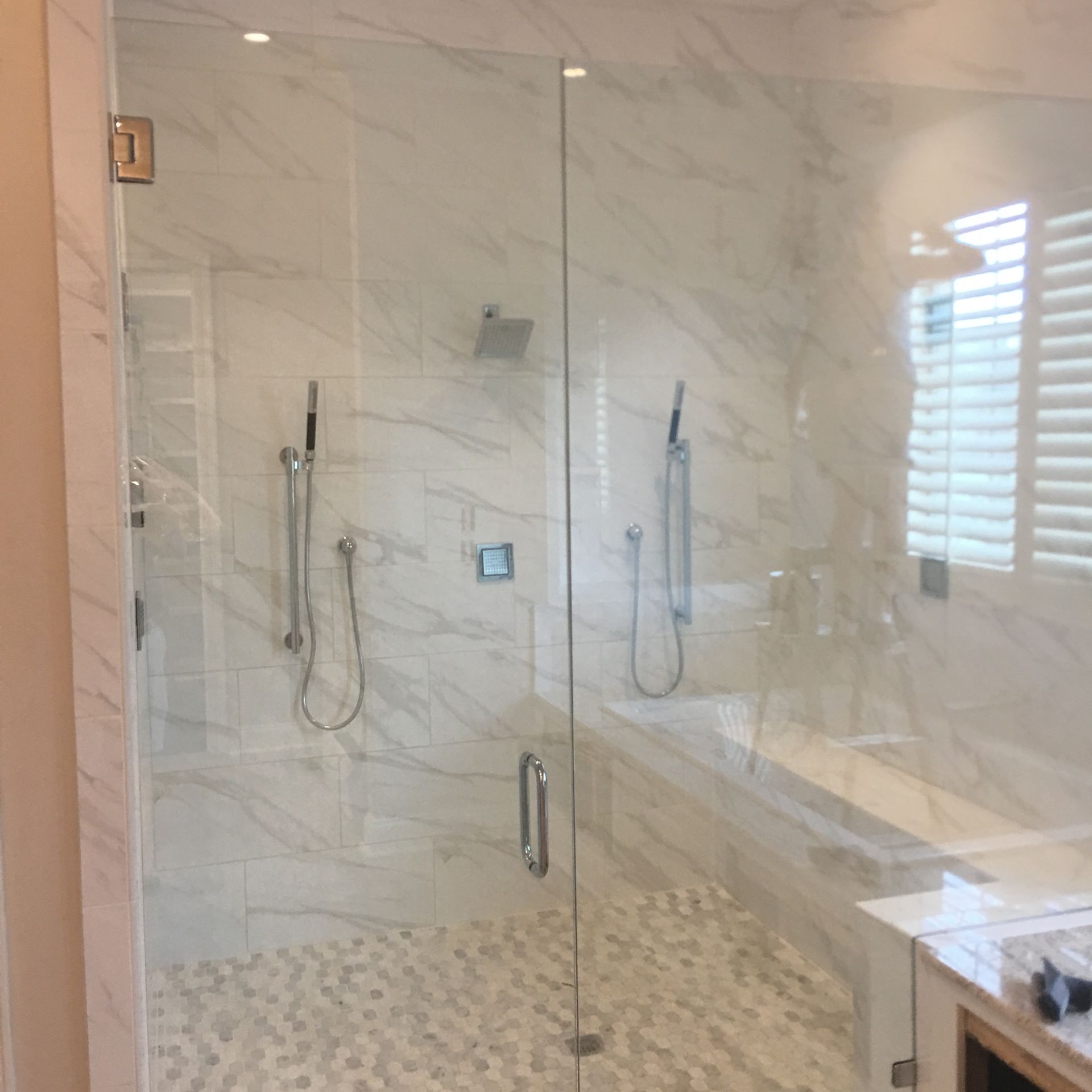 Glass shower with marble tile and pebble floor; handheld showerheads.