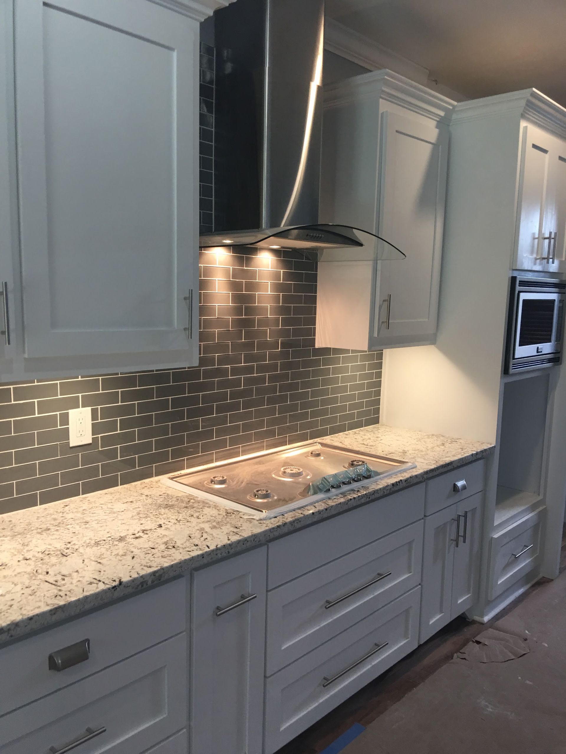 White kitchen with stainless steel appliances, granite countertops, and patterned gray backsplash.