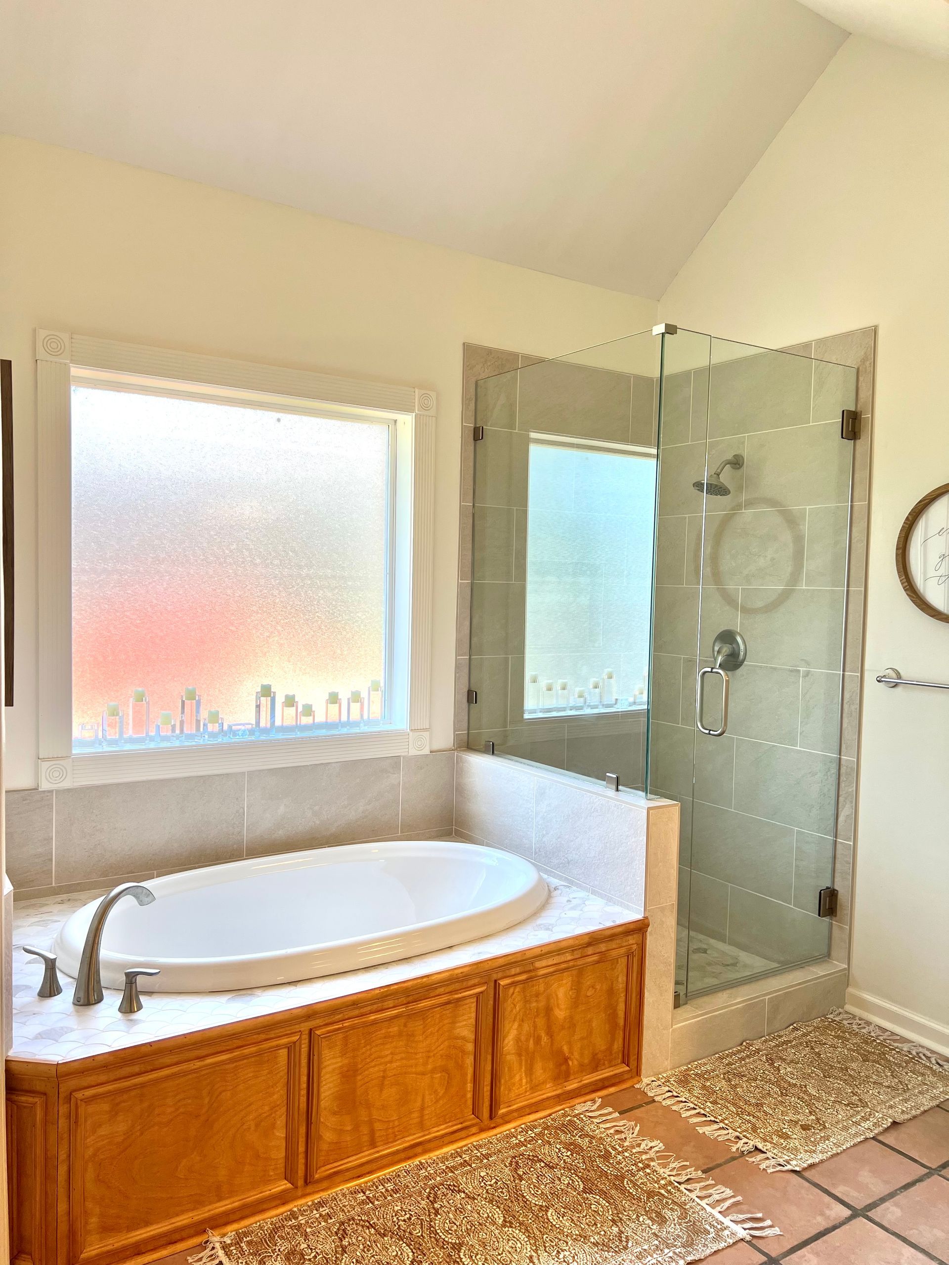 Bathroom with a white tub, glass shower, and window. Warm tones.