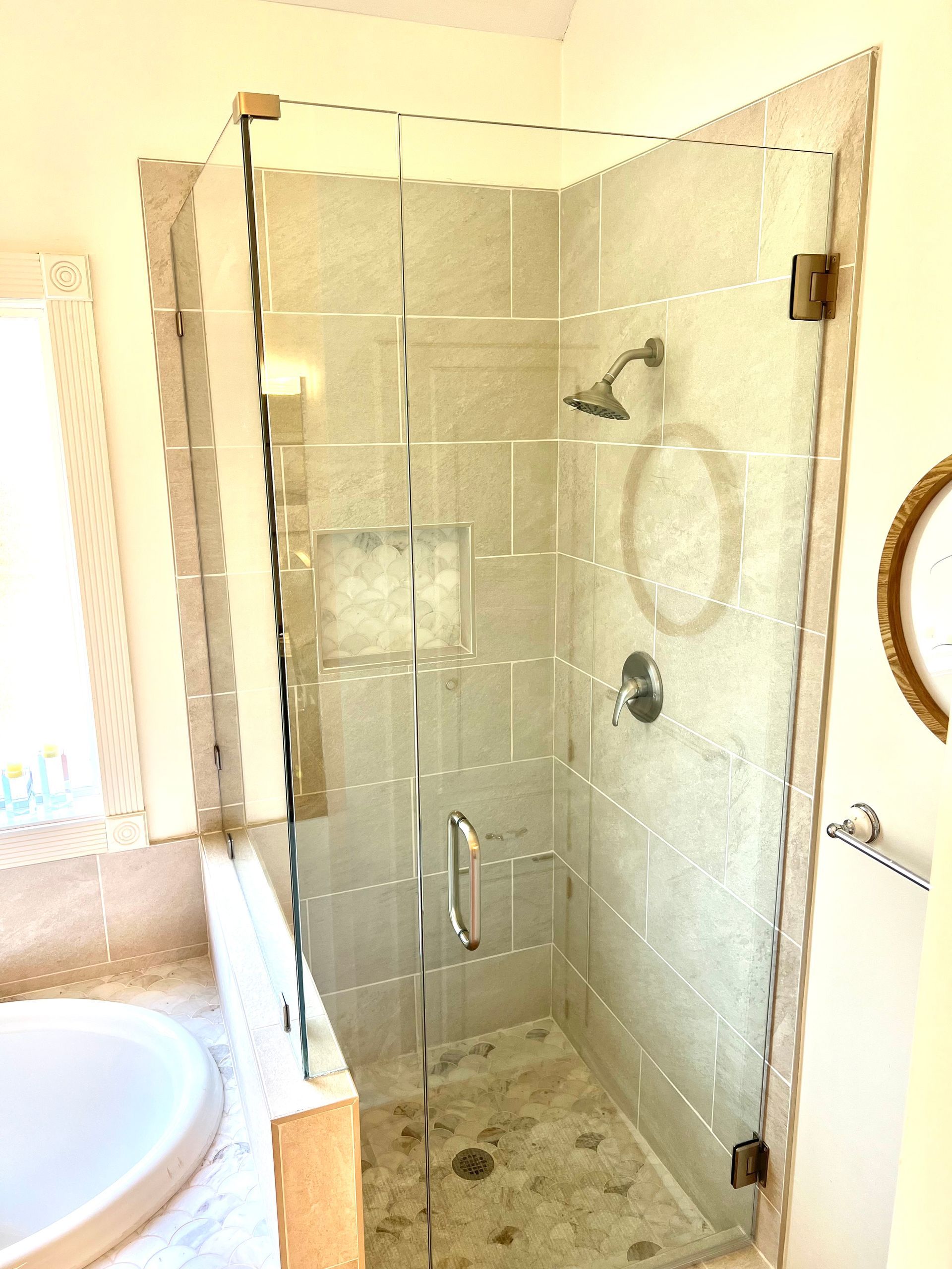 Glass shower enclosure with bronze hardware, on tiled walls and floor, near a sink.