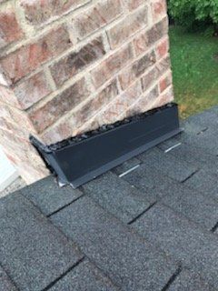 Brick chimney with black flashing on a shingle roof.