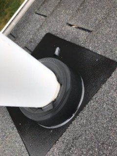 White pipe through a black rubber roof flashing on a gray asphalt shingle roof.