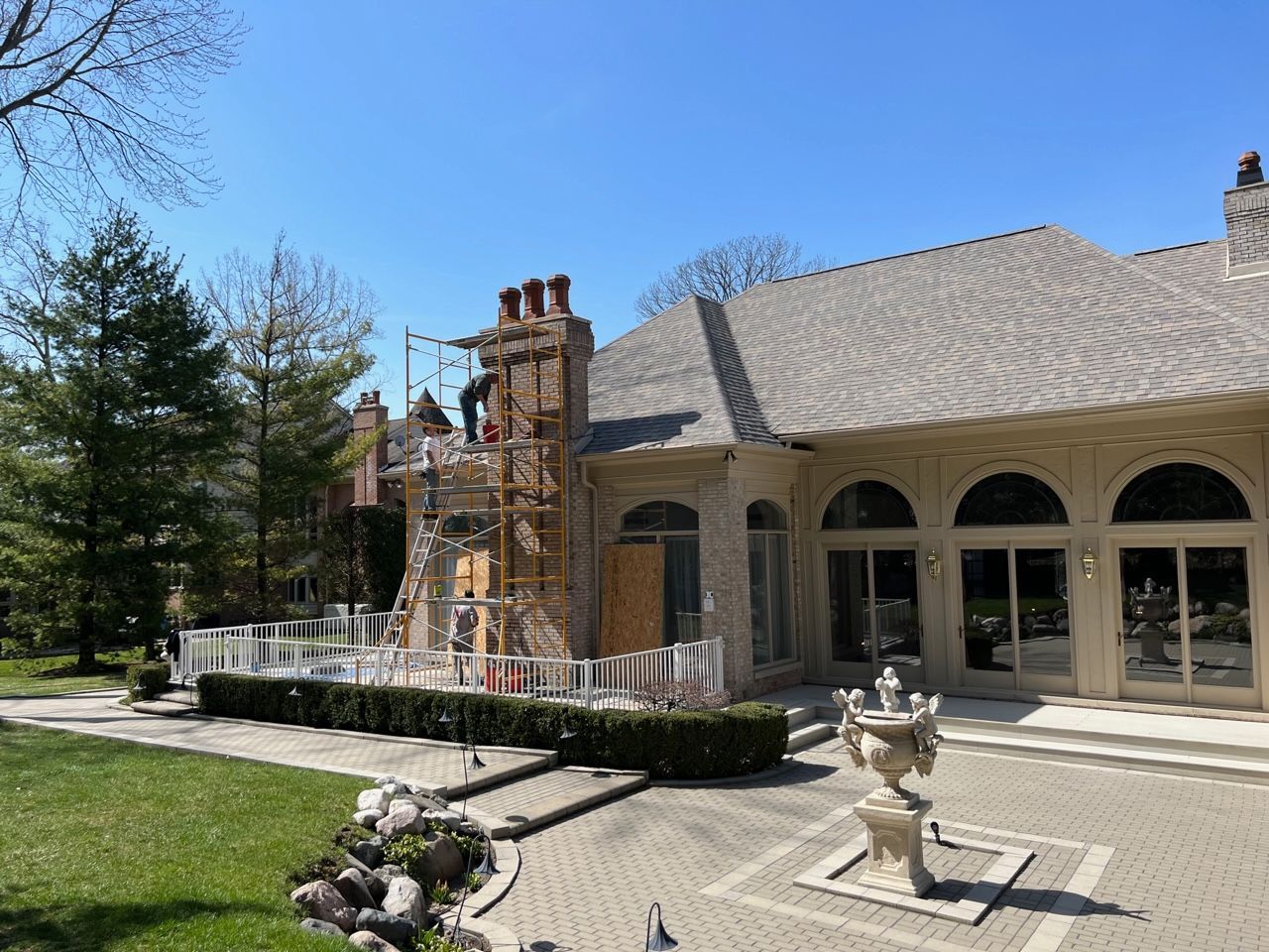 Construction on a large house with scaffolding near the chimney. Two workers are present. Blue sky.