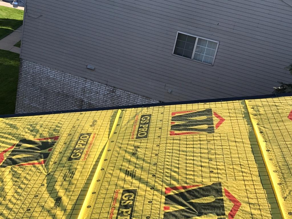Rooftop view with yellow underlayment in foreground, gray roof in background, construction.