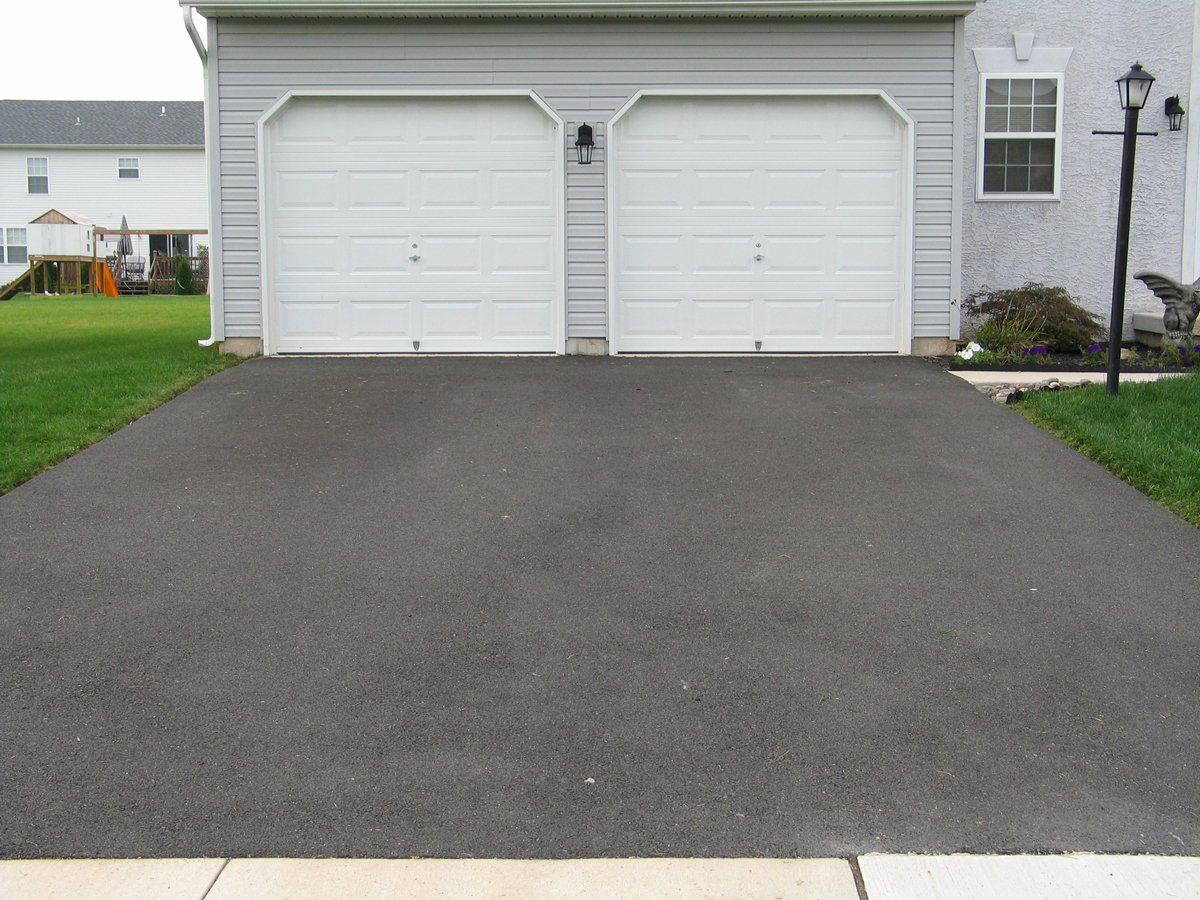 Black asphalt driveway leading to a two-car garage with white doors.