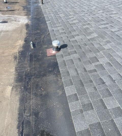 A rooftop with a transition from black asphalt to gray asphalt shingles. A vent is present.