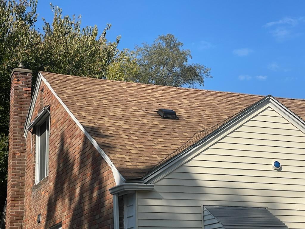 A house with a brown shingle roof, brick chimney, and white siding under a blue sky.
