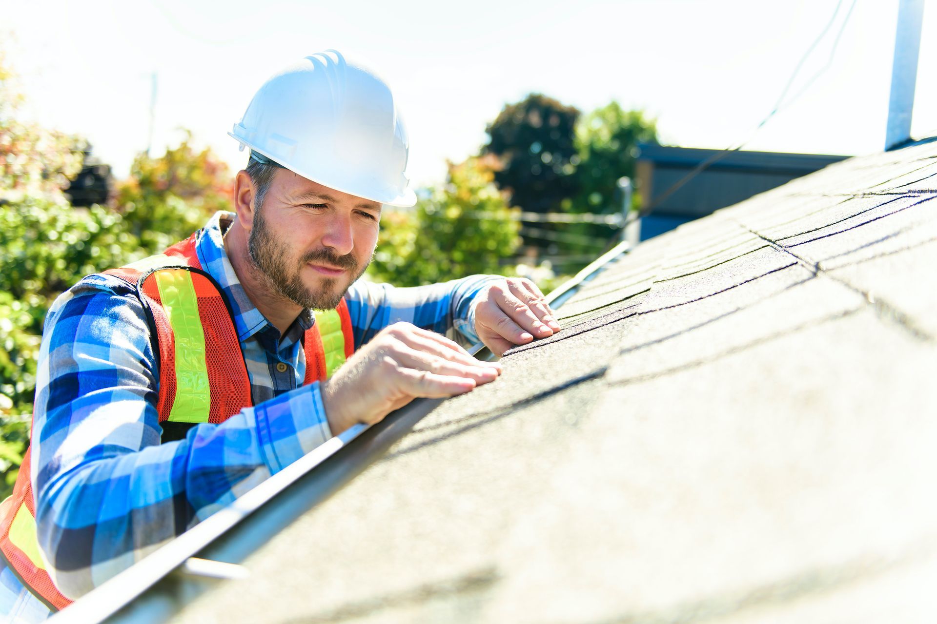 Worker in safety gear inspecting a roof under bright sunlight.