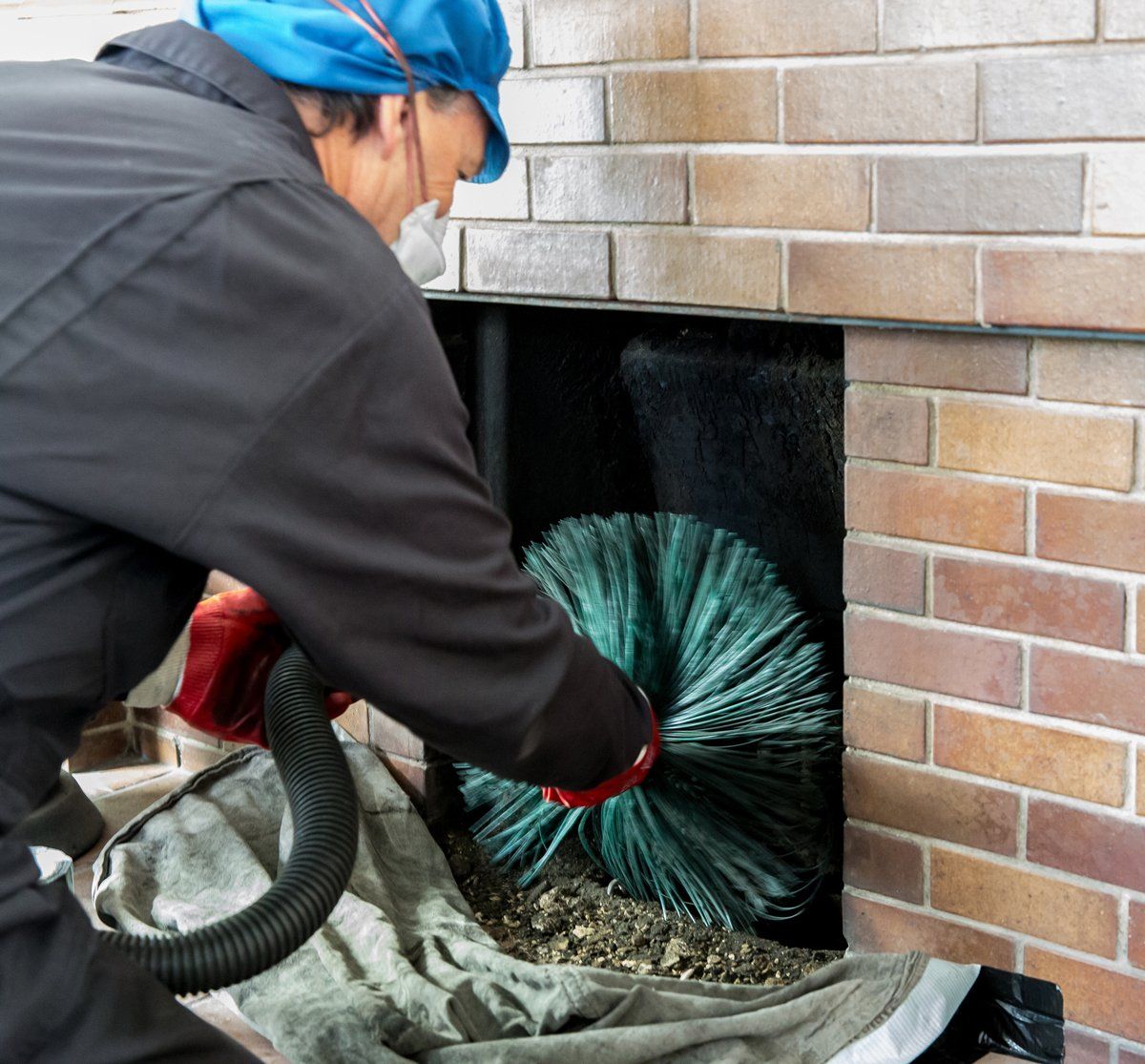 A chimney sweep cleaning a fireplace with a brush and vacuum, brick background.