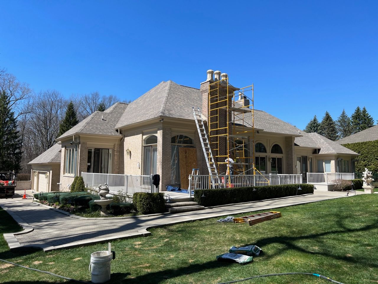 A large stucco home with scaffolding and a ladder for chimney repair on a sunny day.