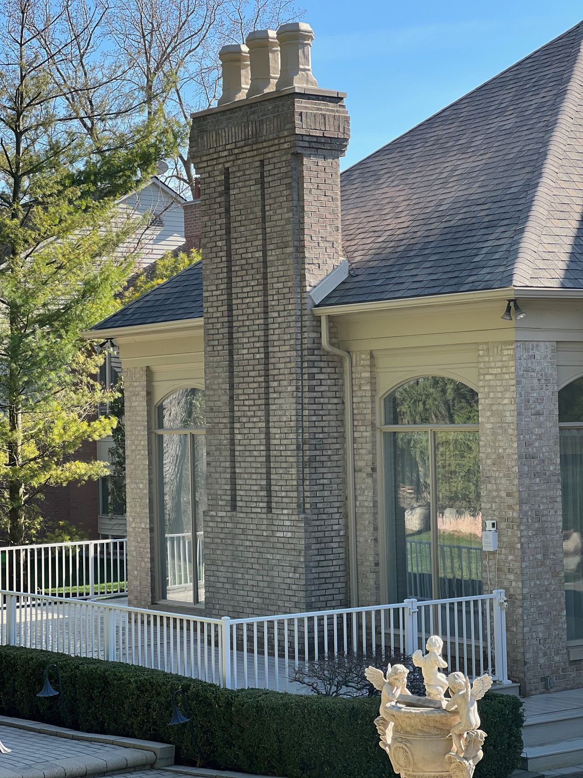 Brick chimney on a house with a white railing and a fountain on a sunny day.