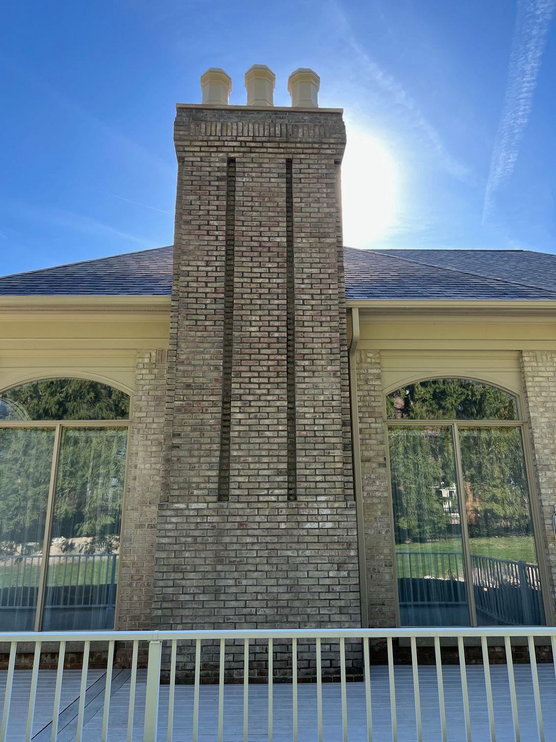Brick chimney with three white top vents, standing on a building with mirrored windows, sunny day.