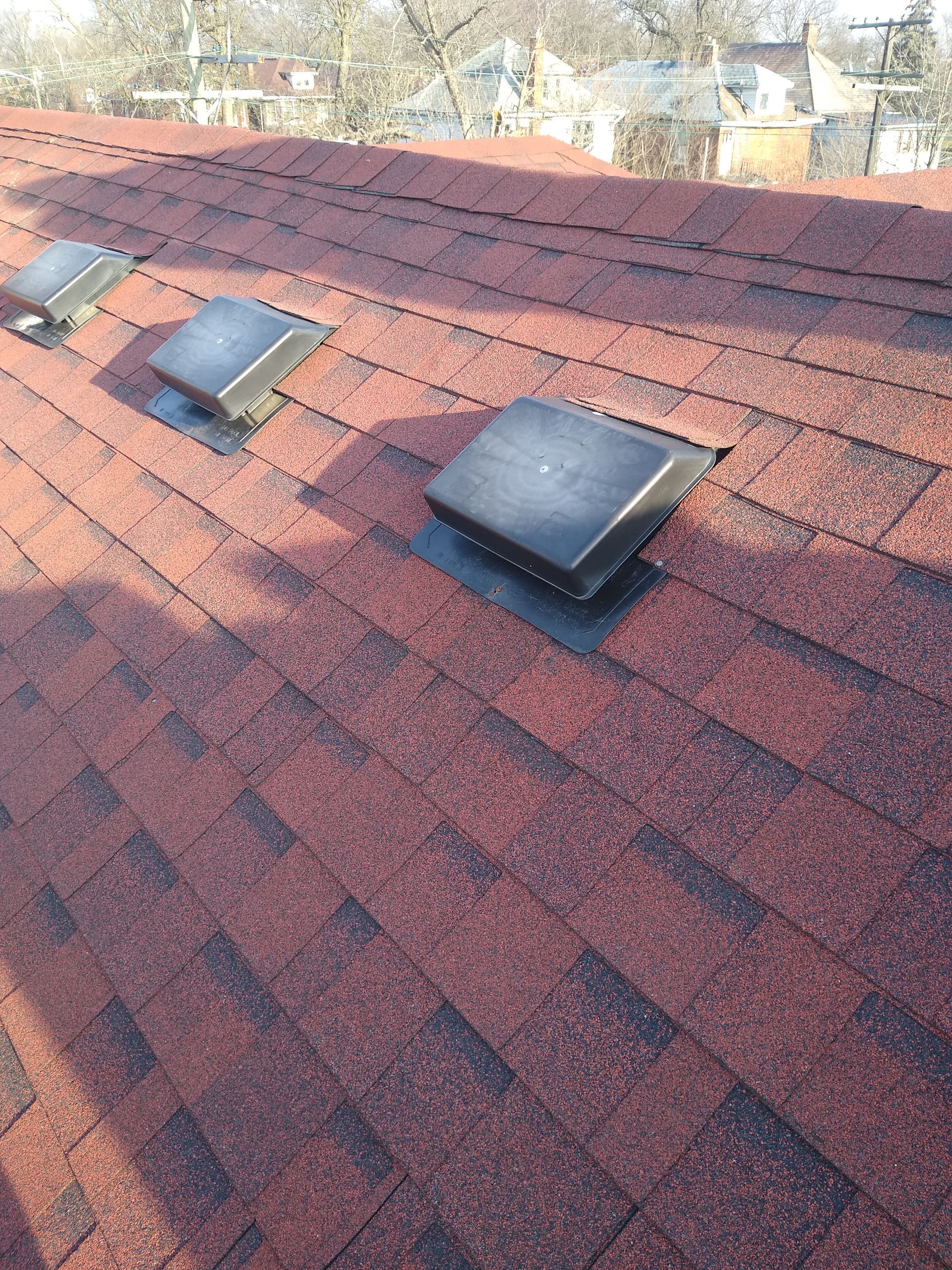 Red shingled roof with three square vents. Sunlight casts shadows.