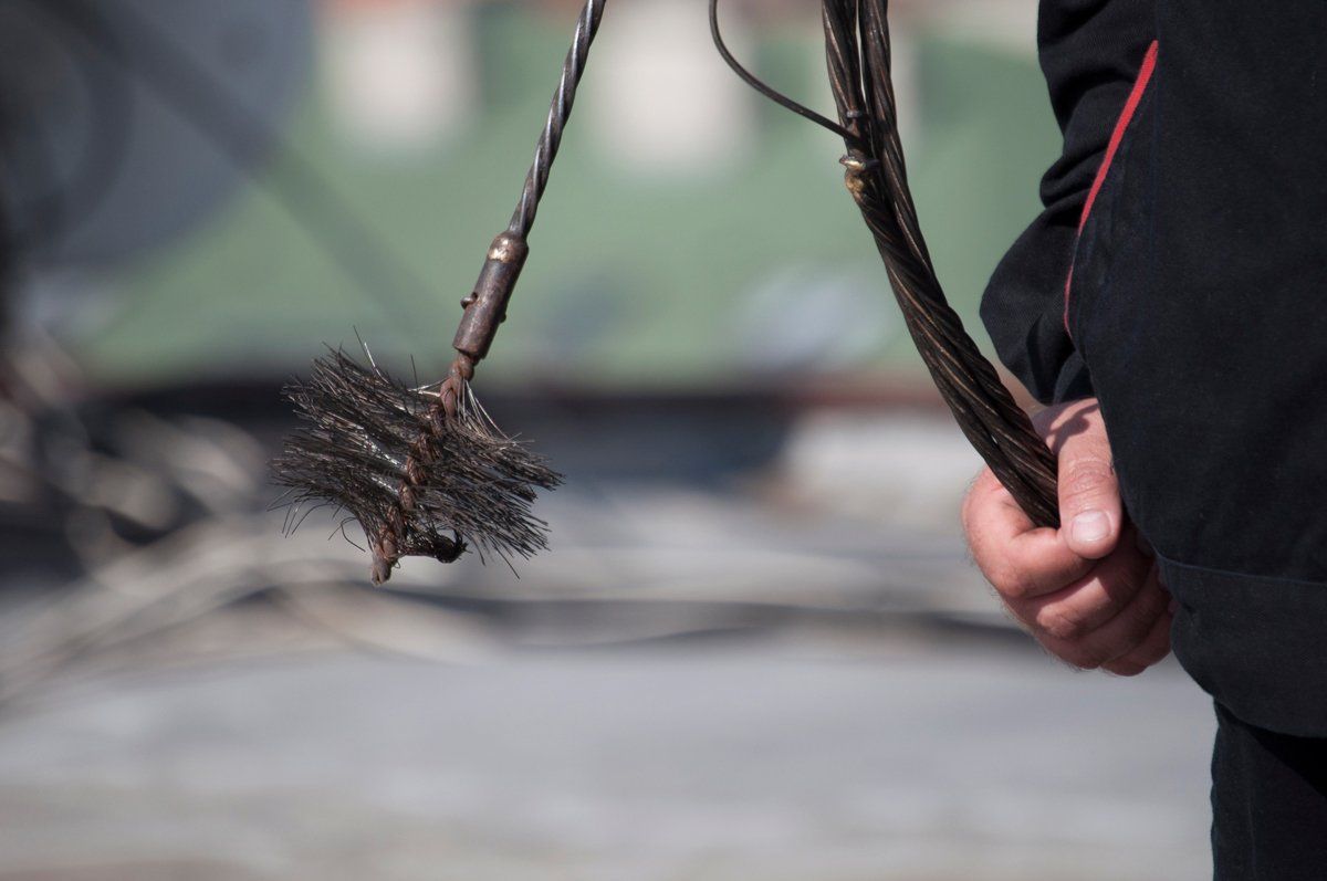 Person holding chimney cleaning brush on a rooftop.