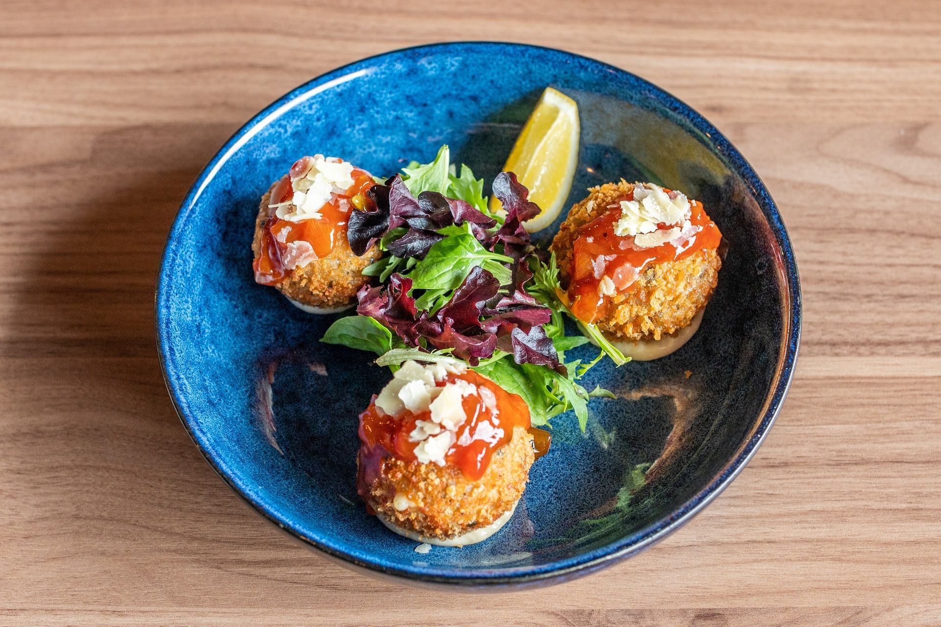 a blue bowl filled with fried Italian food and a lemon wedge