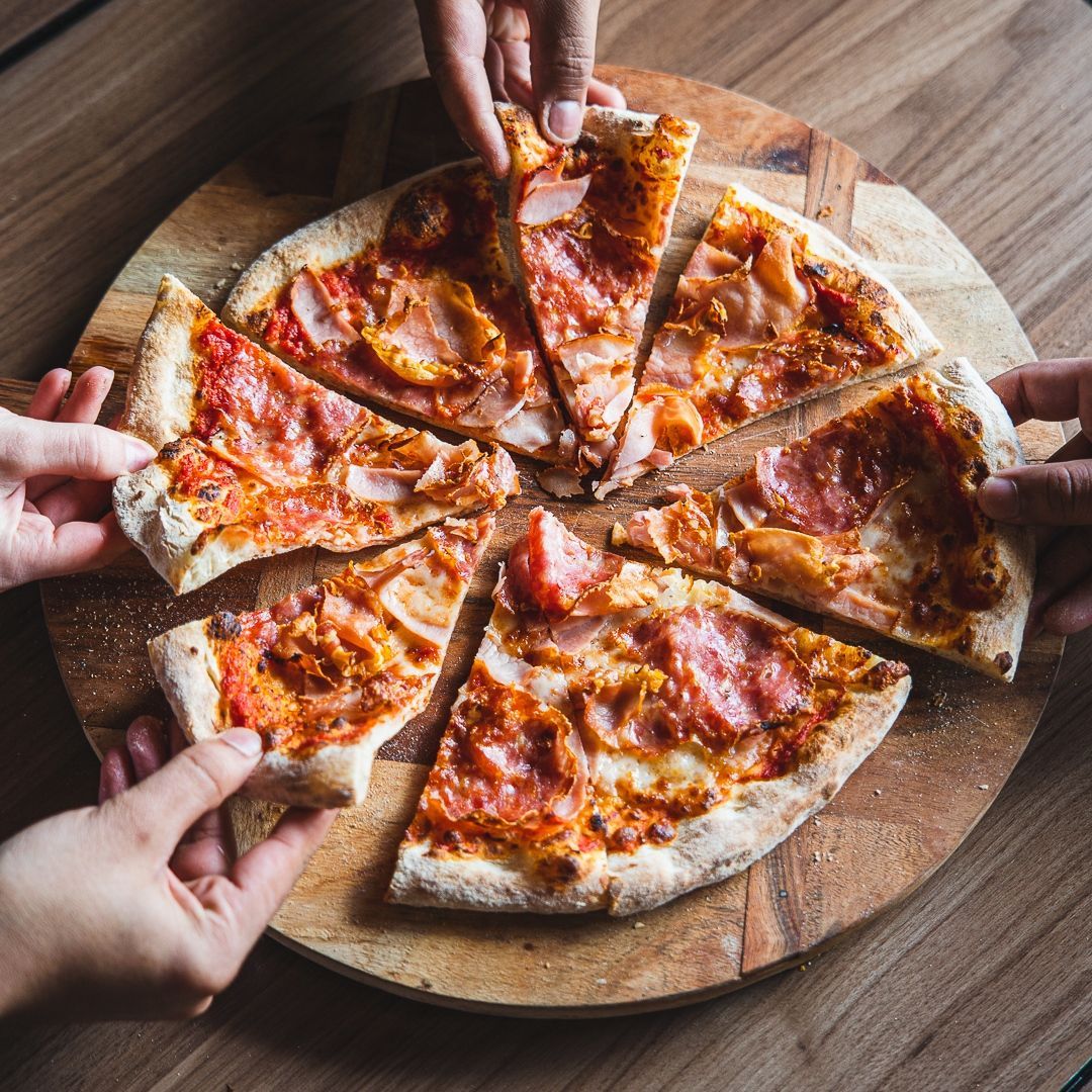 people taking slices of Italian pizza on a wooden cutting board