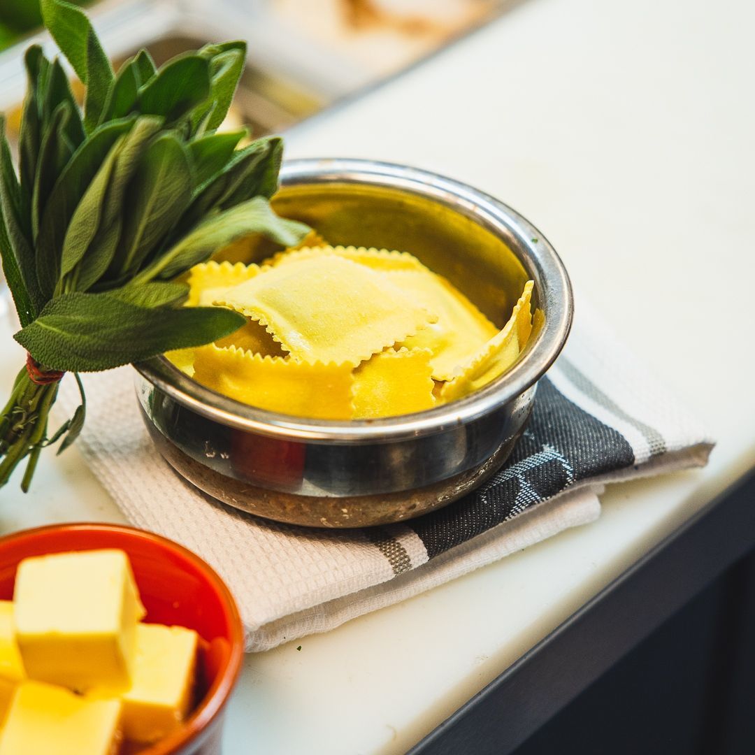 a bowl of ravioli next to a bunch of sage