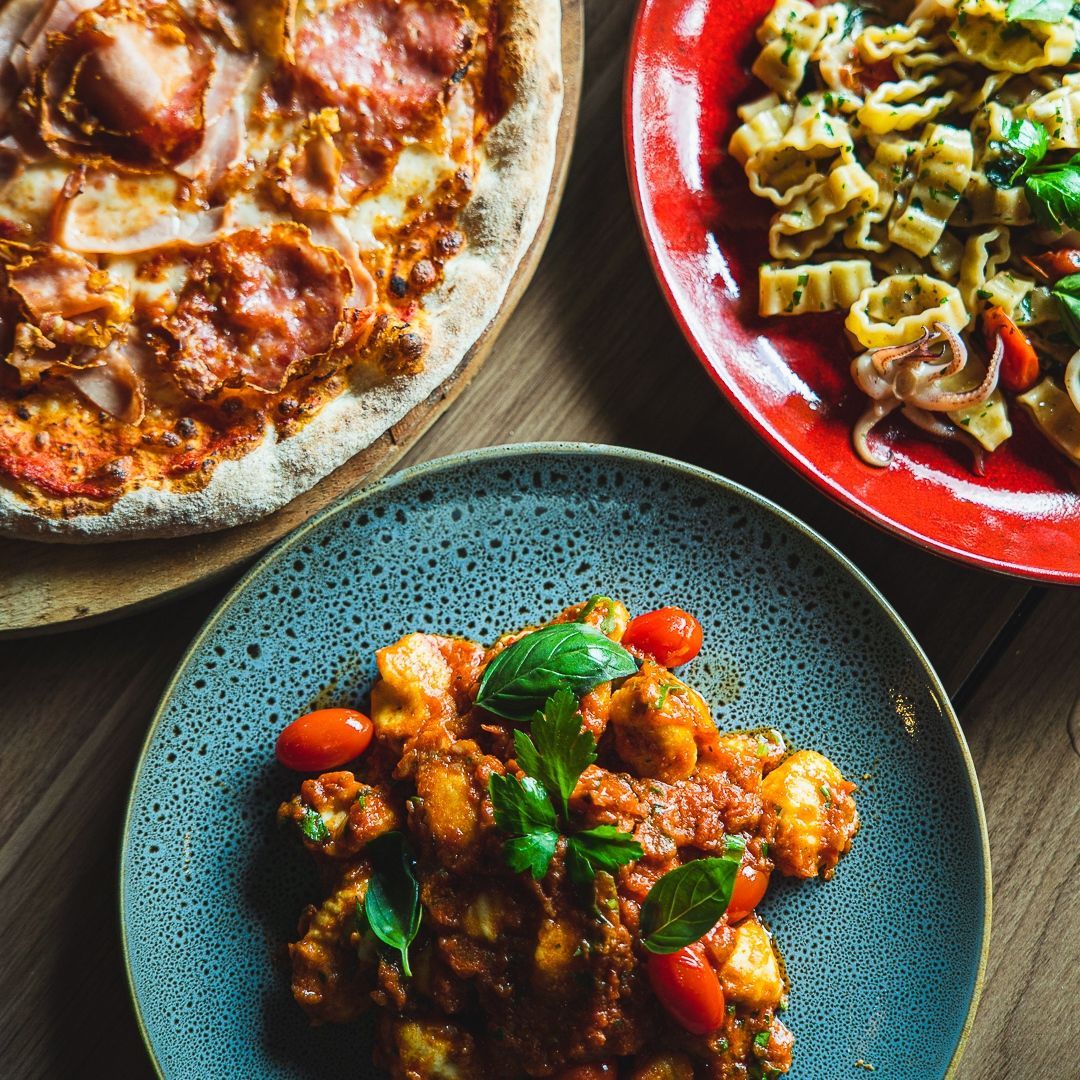 three plates of food on a table including a pizza and pasta