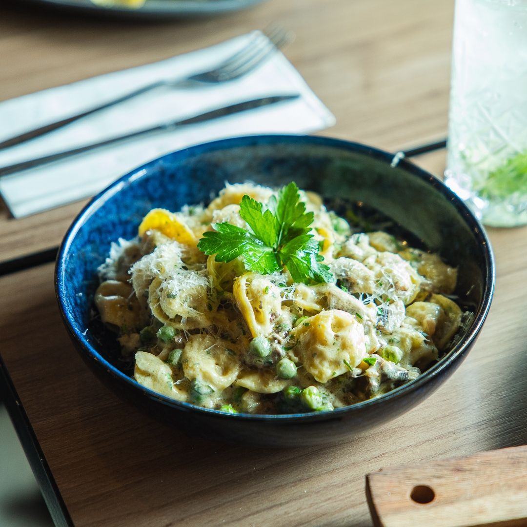 a bowl of tortellini pasta with peas and parsley on top
