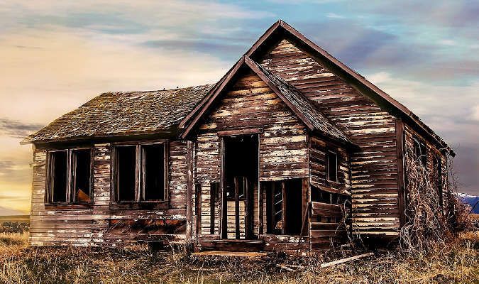 An old wooden house is sitting in the middle of a field.