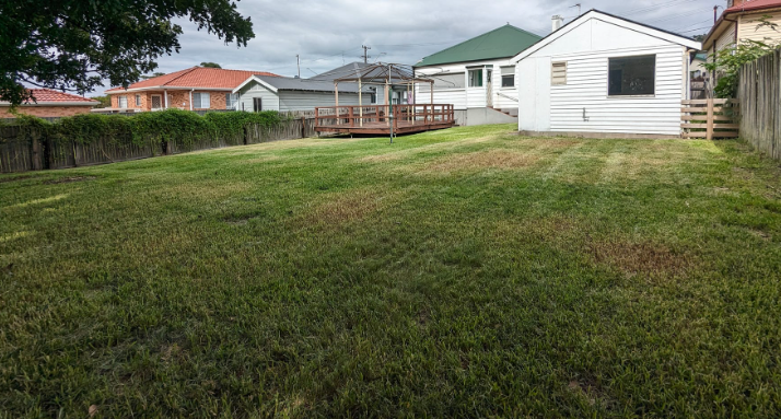 A Wheelbarrow Filled With Grass Is Parked In Front Of A House — Roots, Shoots & Leaves Garden Maintenance In East Corrimal, NSW