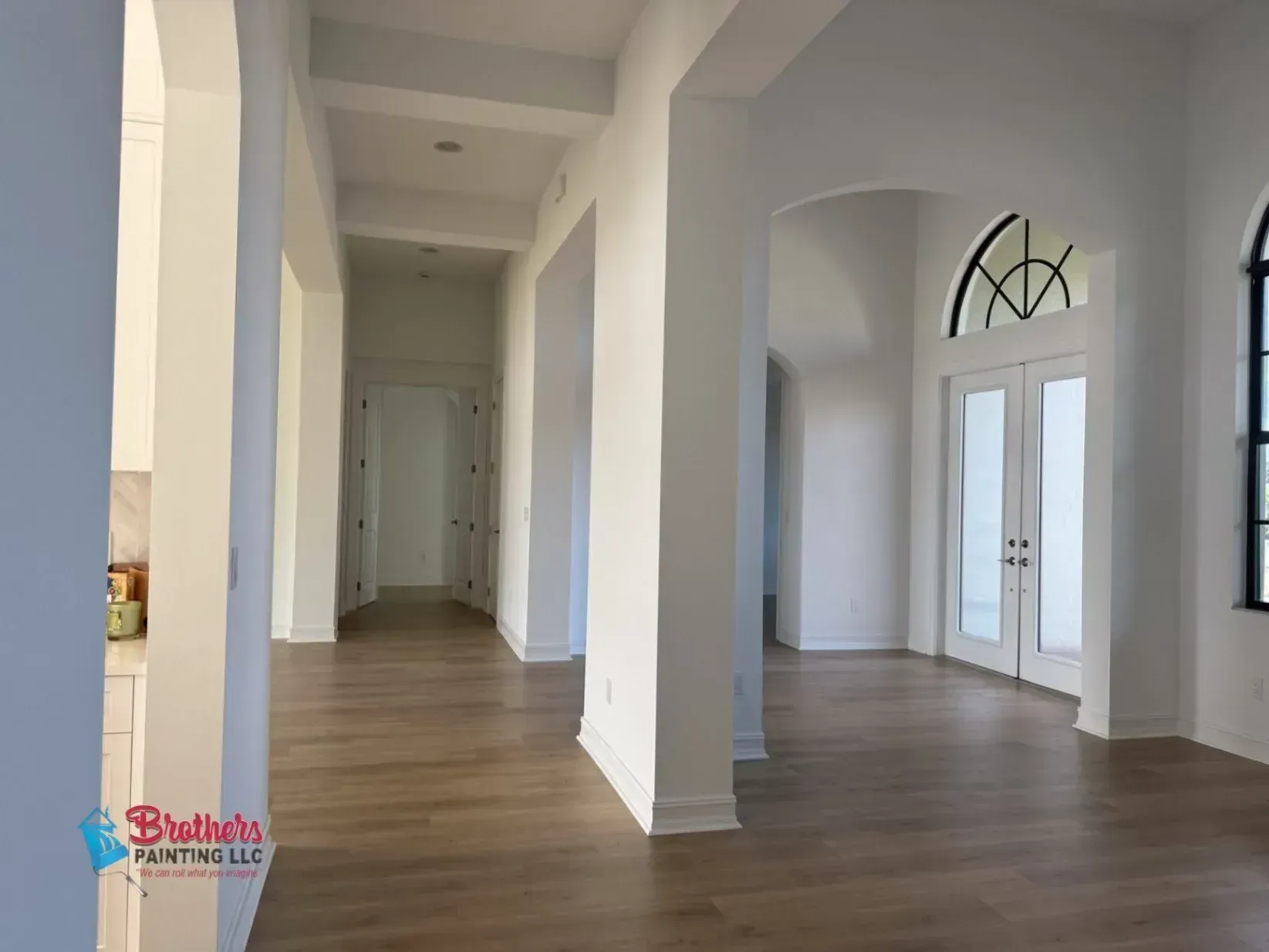 Bright empty hallway with white arches, tall windows, and wood floors
