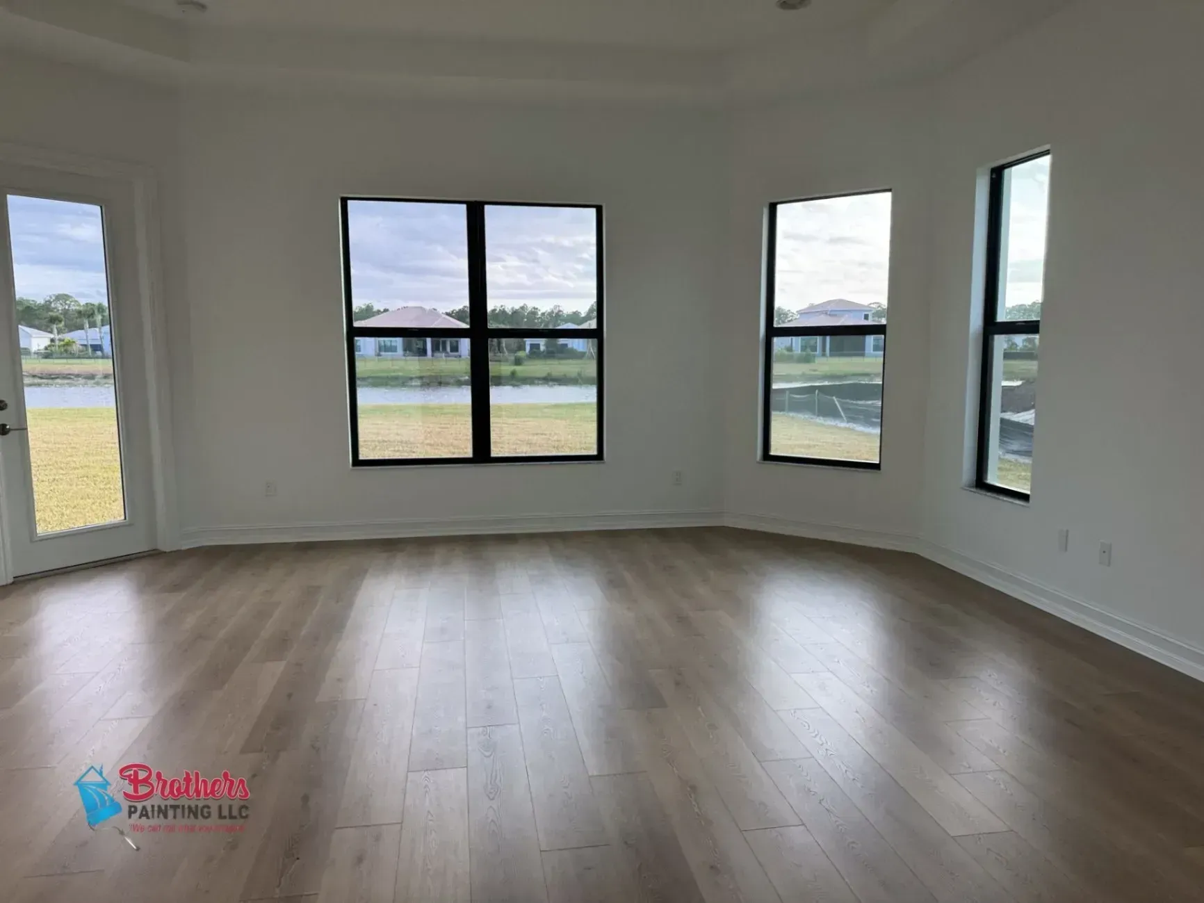 Empty modern living room with light wood floors and large windows overlooking a grassy field