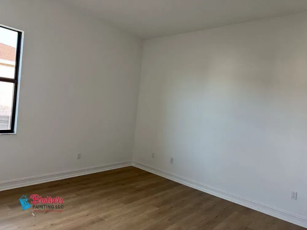 Empty white room with wood floors and a window on the left.
