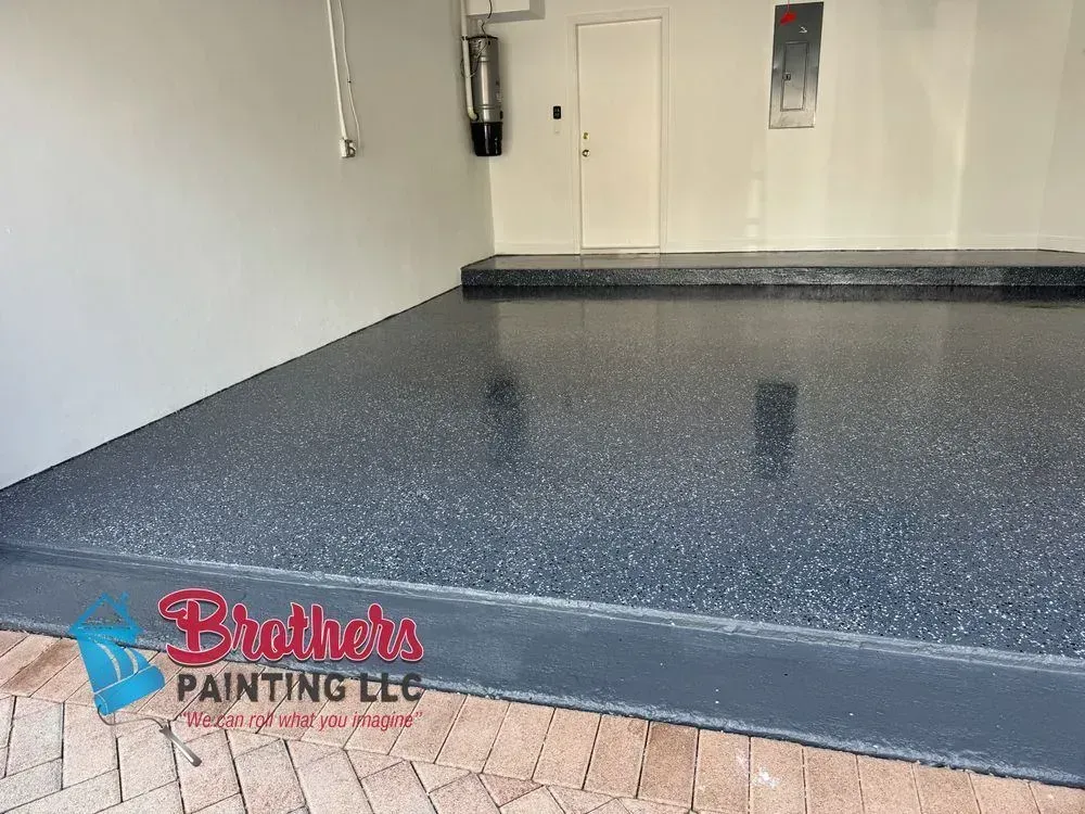 Freshly coated dark speckled garage floor in an empty room with a door and wall fixture