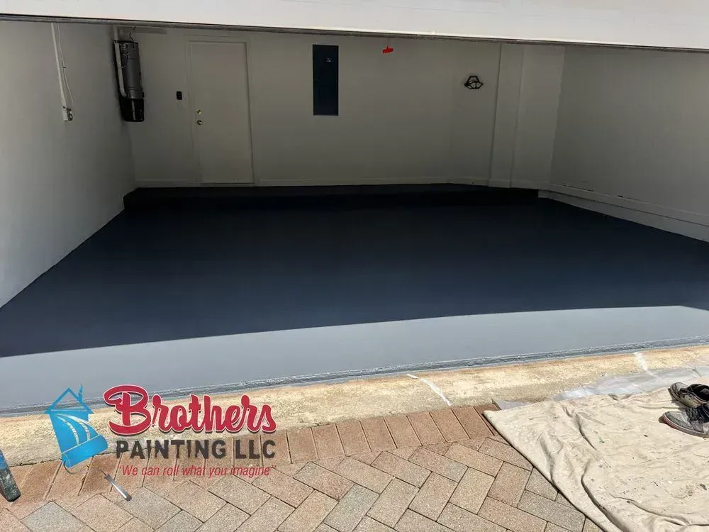 Empty garage with freshly painted dark gray floor and white walls, showing a painting company watermark.