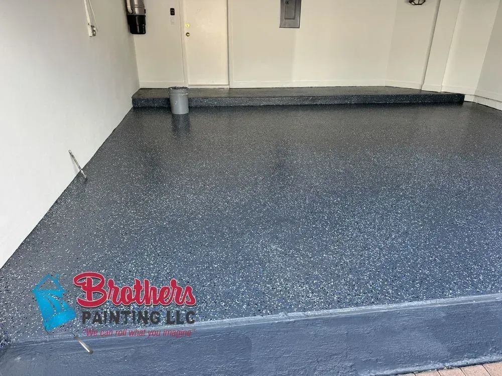 Empty garage floor with gray speckled epoxy coating and a Brothers Painting LLC logo