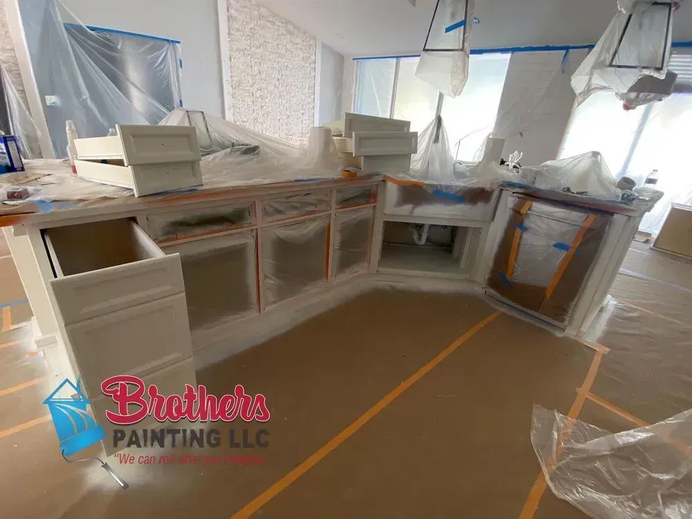 Painted kitchen cabinets in a room under renovation, with white trim and protective plastic sheeting.