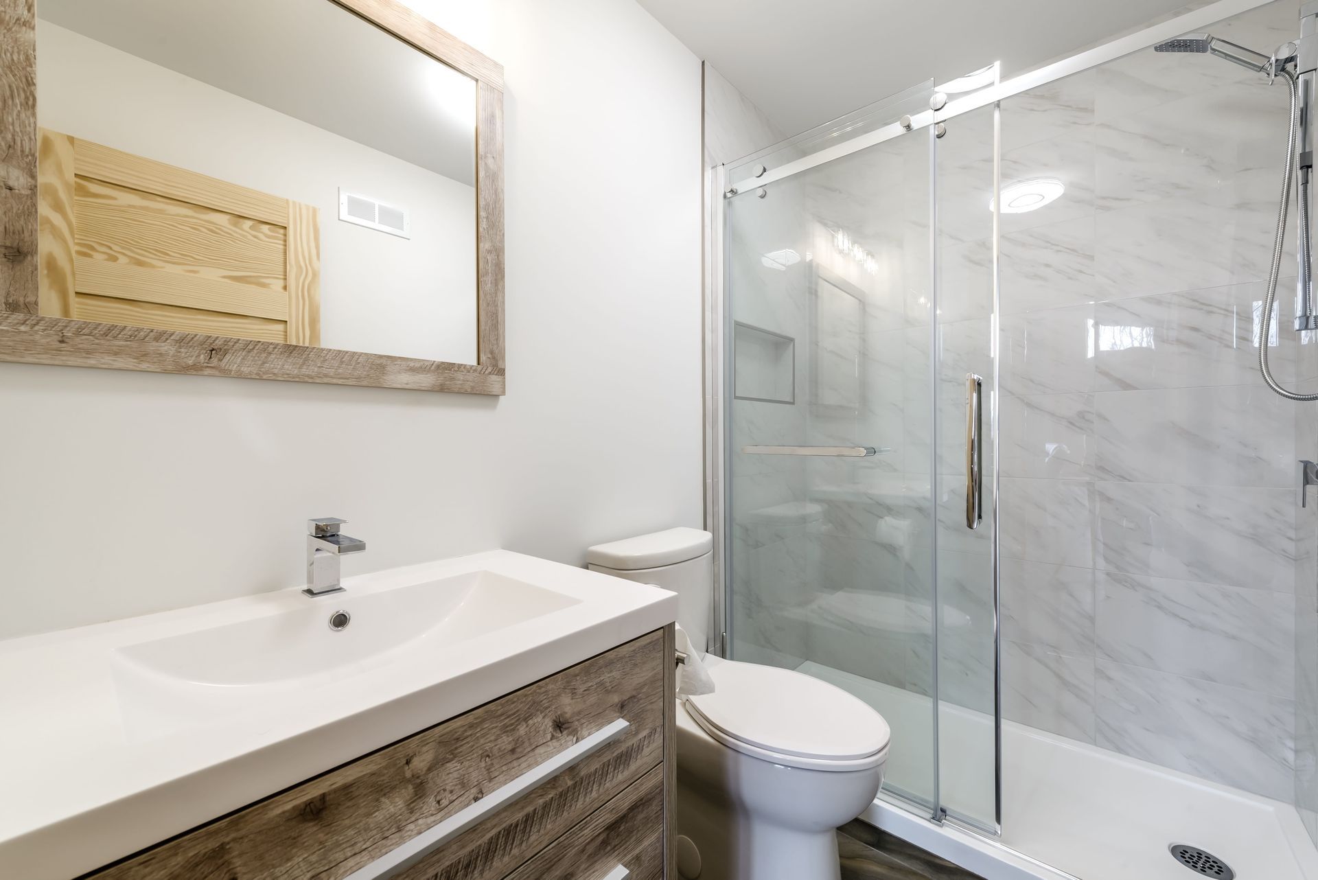 Modern bathroom with a rustic wooden vanity, a white countertop sink, a framed mirror, and a glass-enclosed shower.