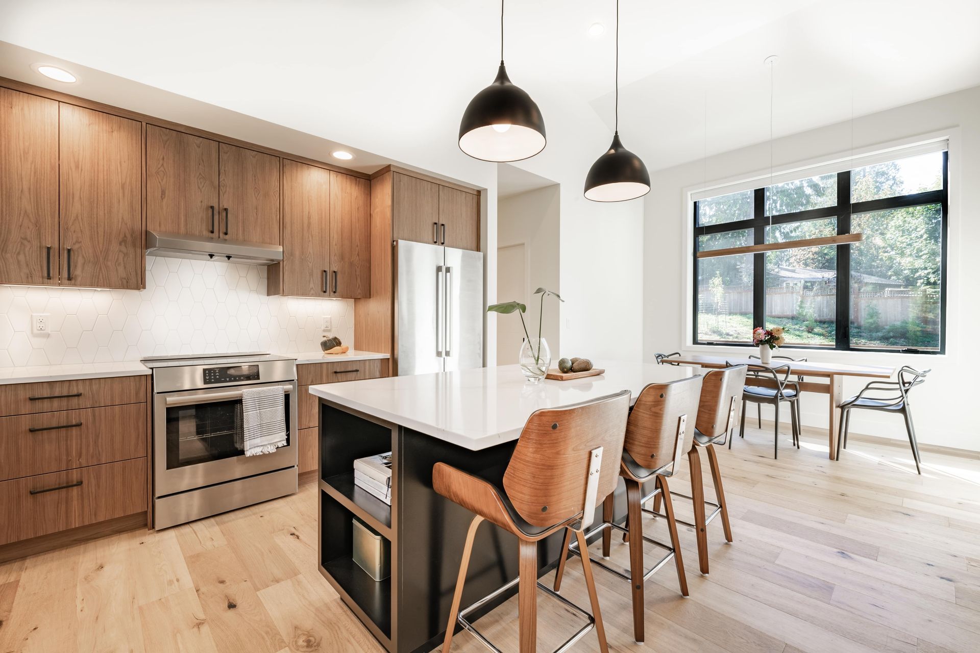 A modern kitchen featuring wooden cabinets, a white island with bar stools, stainless appliances, and a dining area.