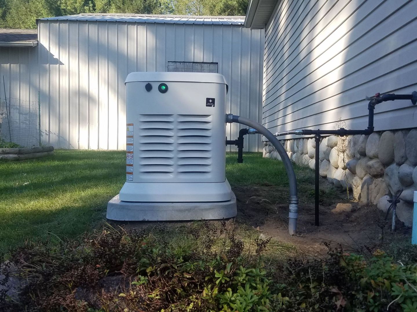 A white generator is sitting on the side of a house.